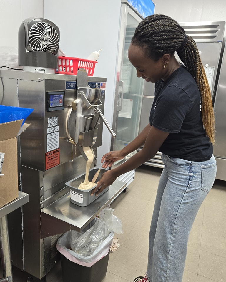 Woman using a machine to dispense liquid into a container in a kitchen or laboratory setting.