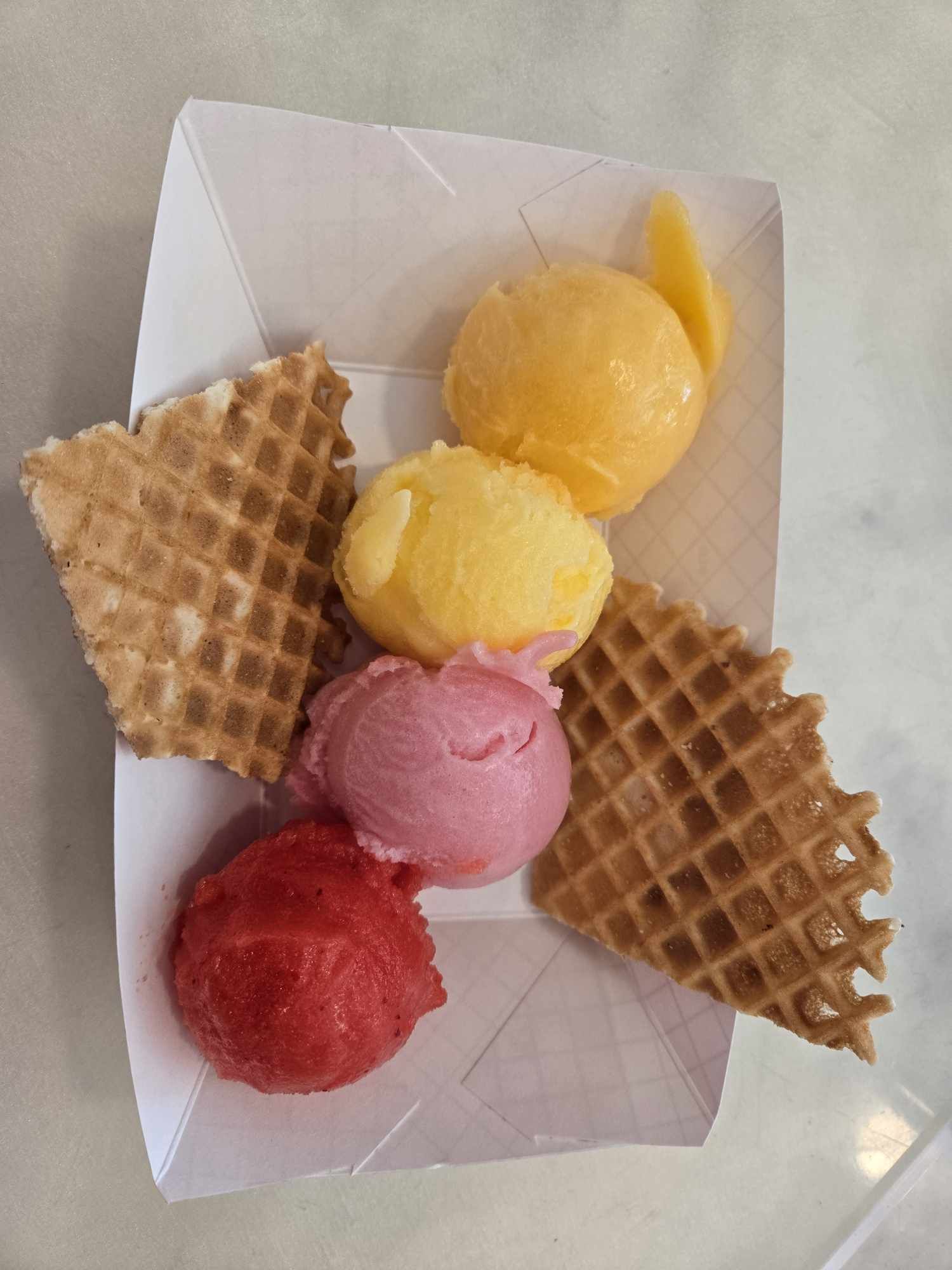 Four scoops of colorful ice cream with waffle pieces in a white tray.