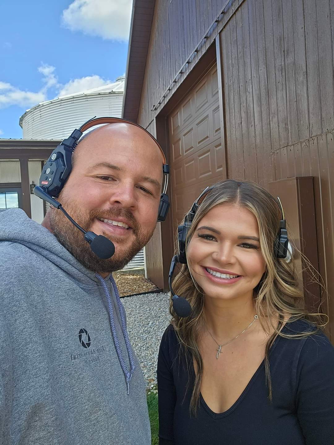 Two people wearing headsets smiling outdoors near a building with a blue sky background.