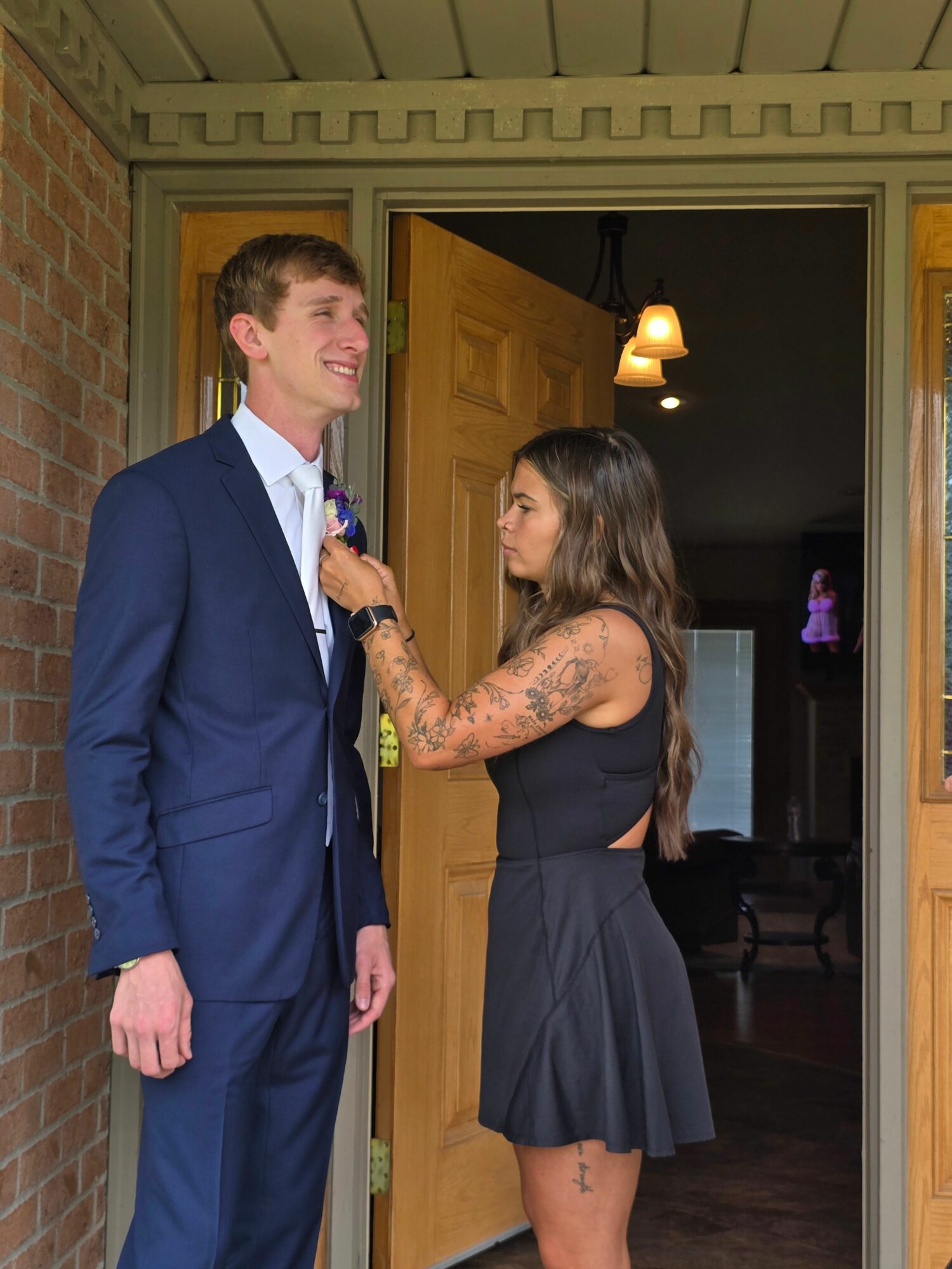 Woman with tattoos holding microphone and talking to man in suit outside doorway.