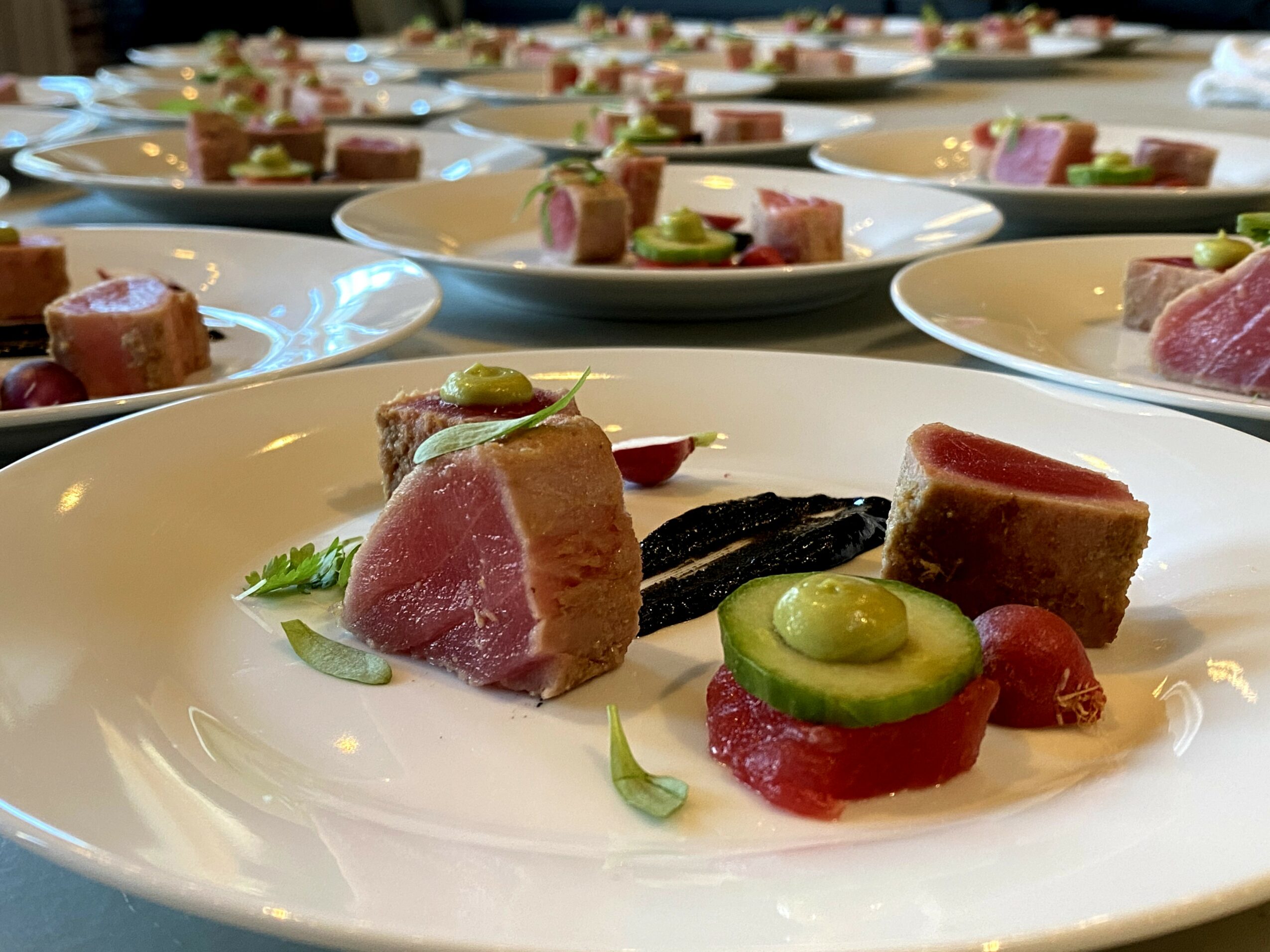Multiple plates with slices of meat, green sauce, and garnishes arranged on a table.