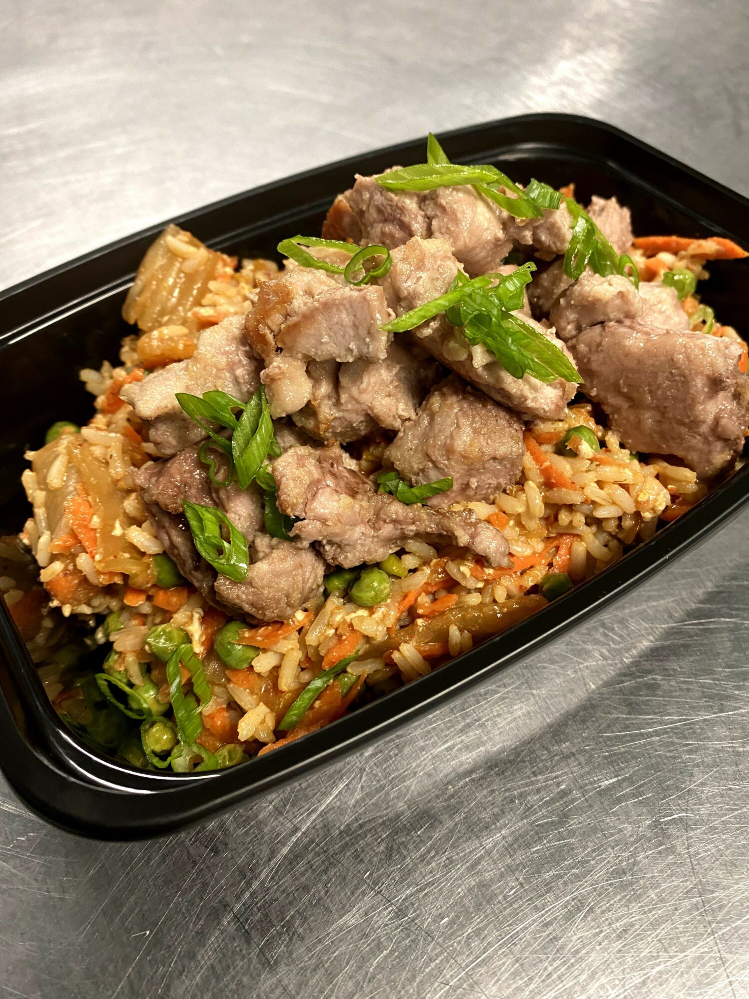 Fried rice with vegetables and sliced beef garnished with green herbs in a black container.