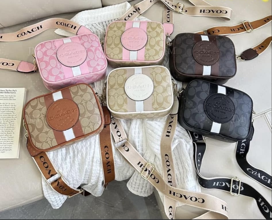 Six small Coach bags in pink, beige, brown, and black with straps, arranged on a surface with some fabric and tags.