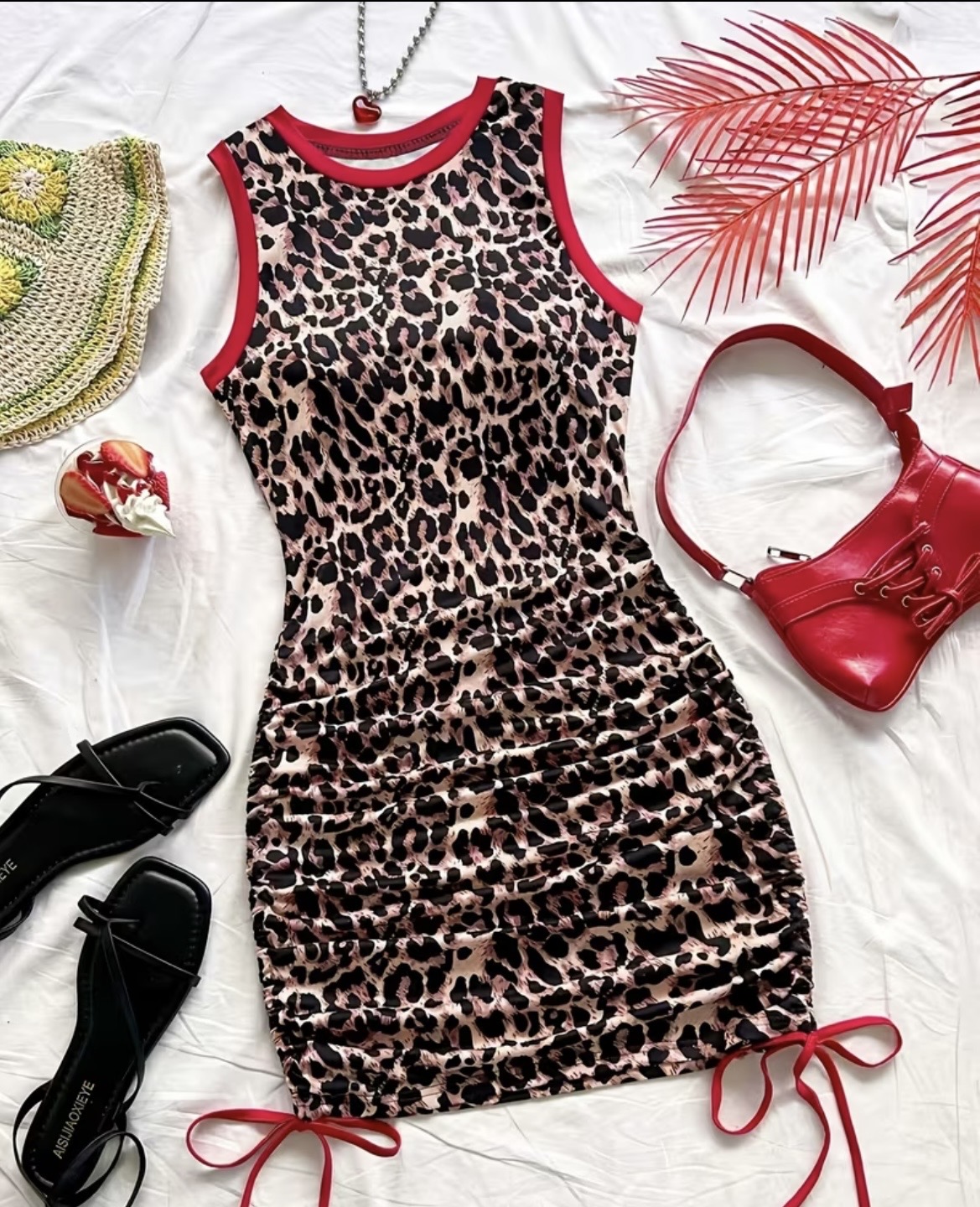 Leopard print sleeveless dress with red trim, tied at the bottom, surrounded by accessories and decorative items.