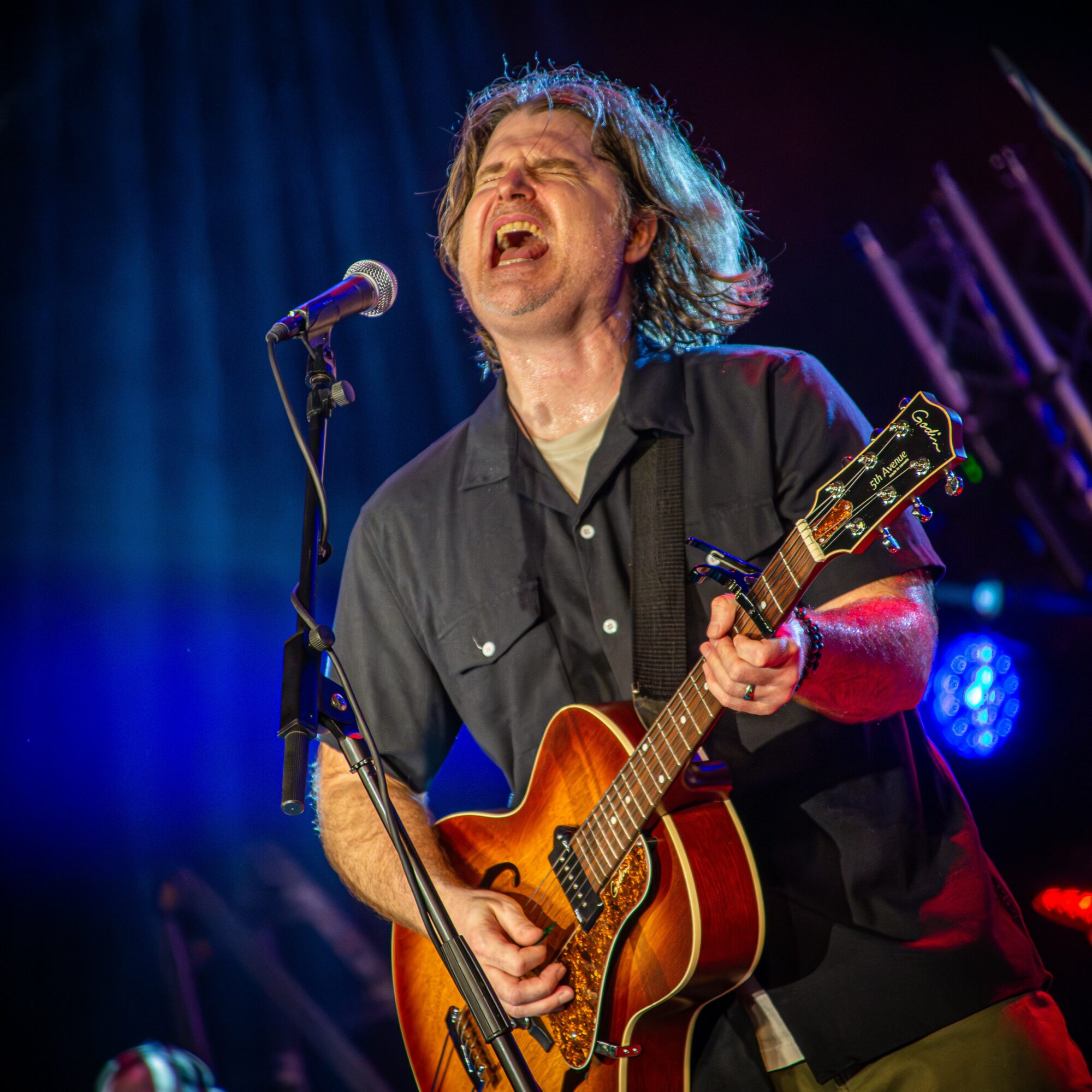 Man singing passionately while playing an acoustic guitar on stage with colorful lighting.