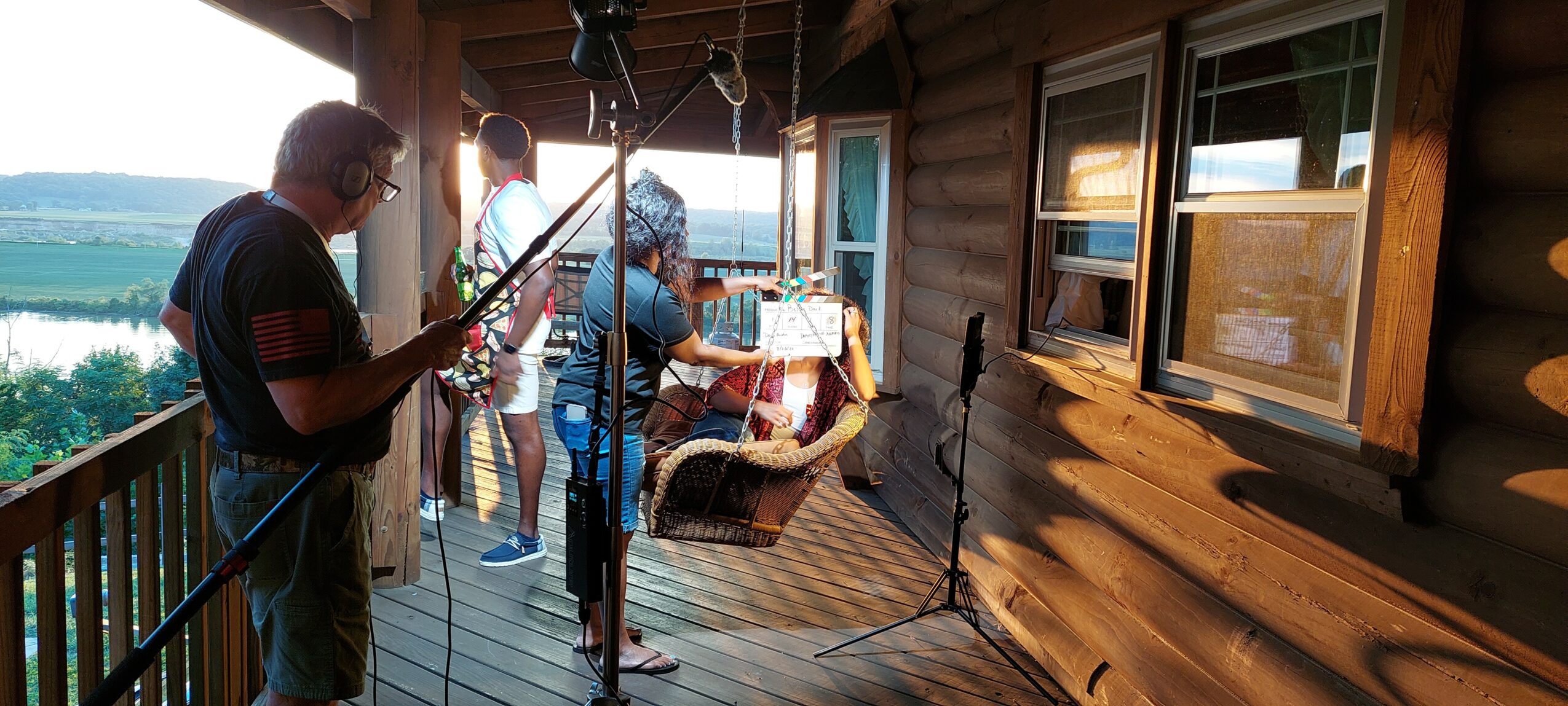 People gather on a wooden porch with a view of water and trees in the background.
