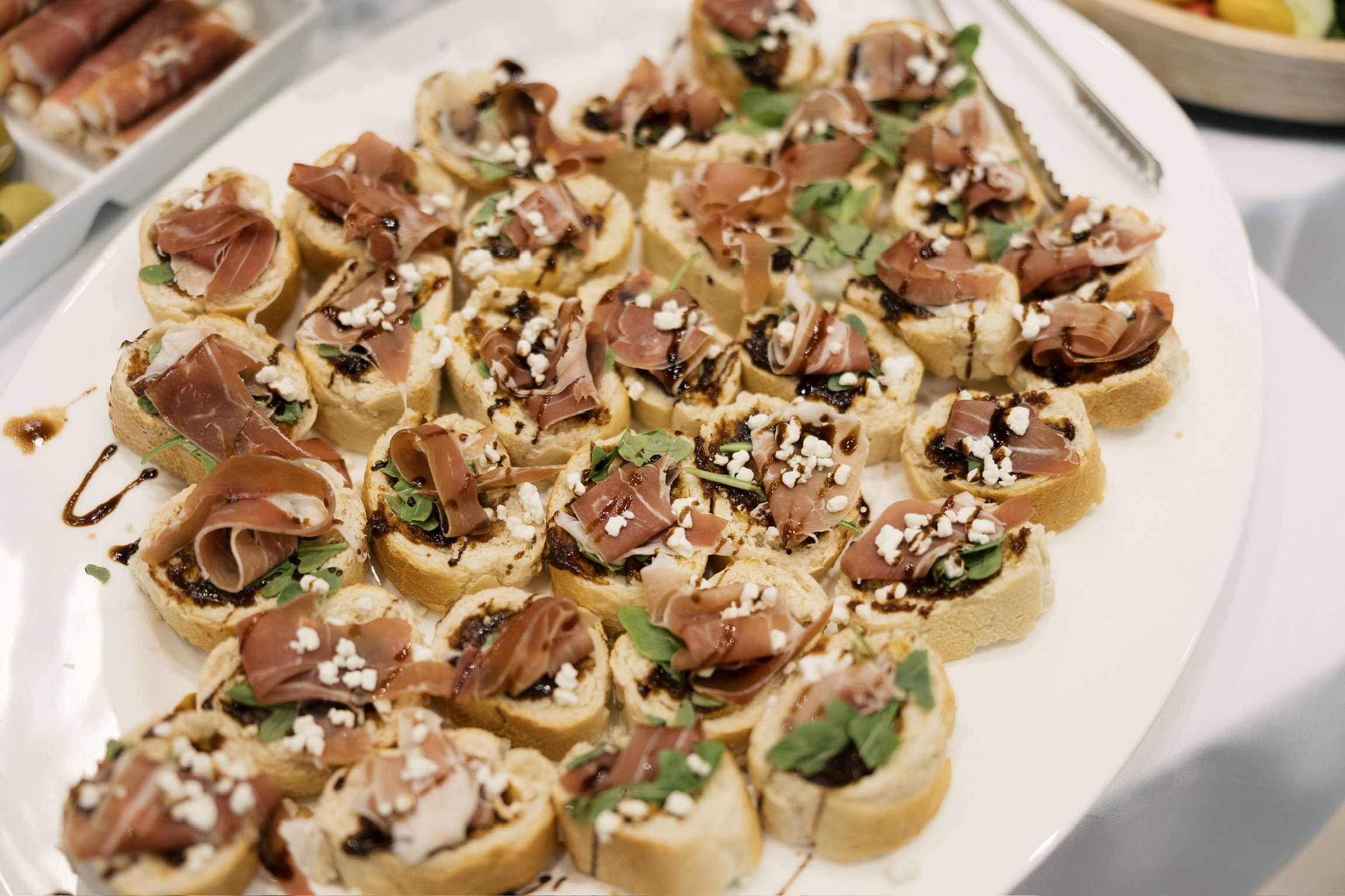 Plate of small appetizers with sliced meat, herbs, and toppings, arranged on a white dish.