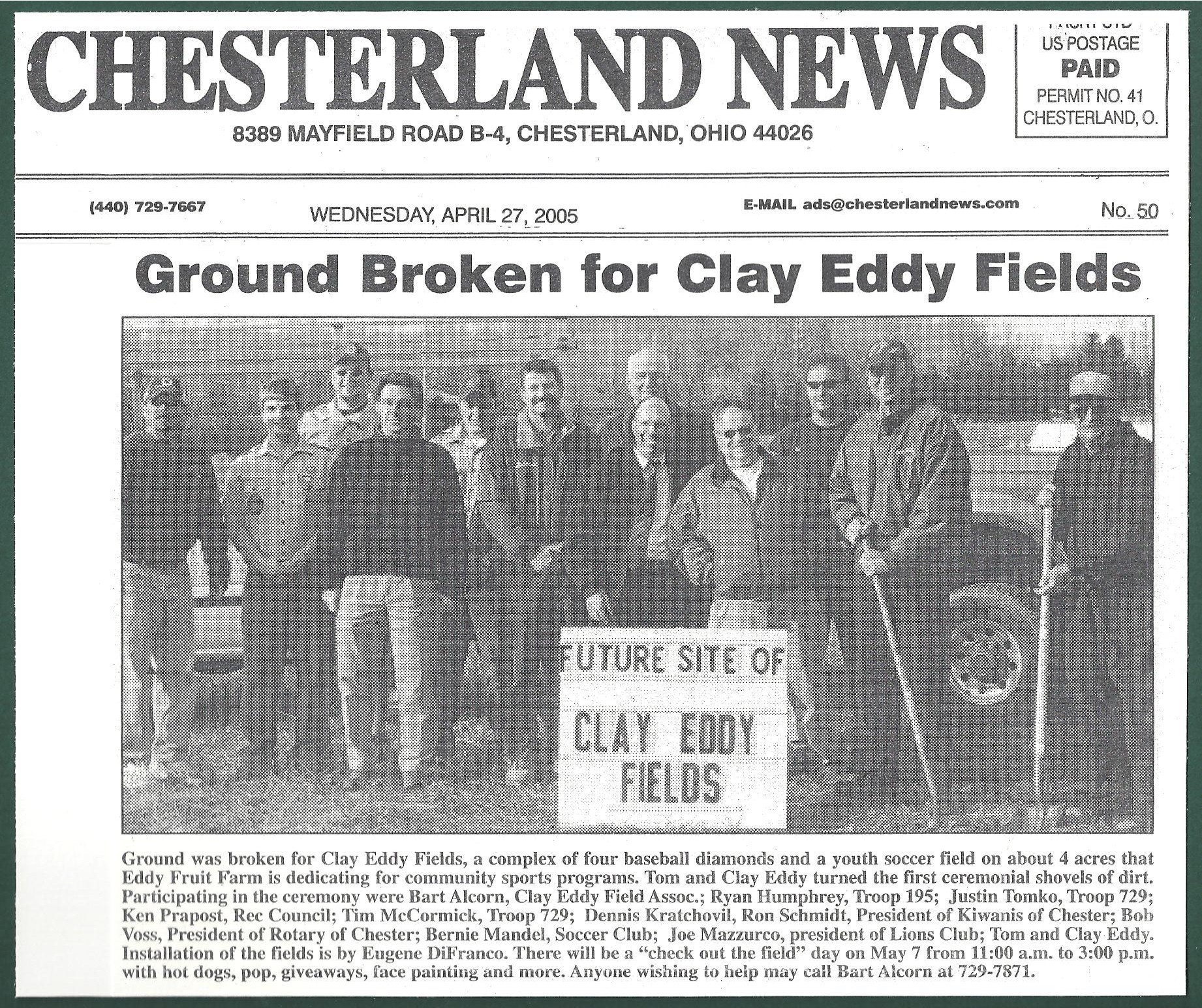 Group of people standing outdoors in front of a car, holding a sign that reads 'Future Site of Clay Eddy Fields.'