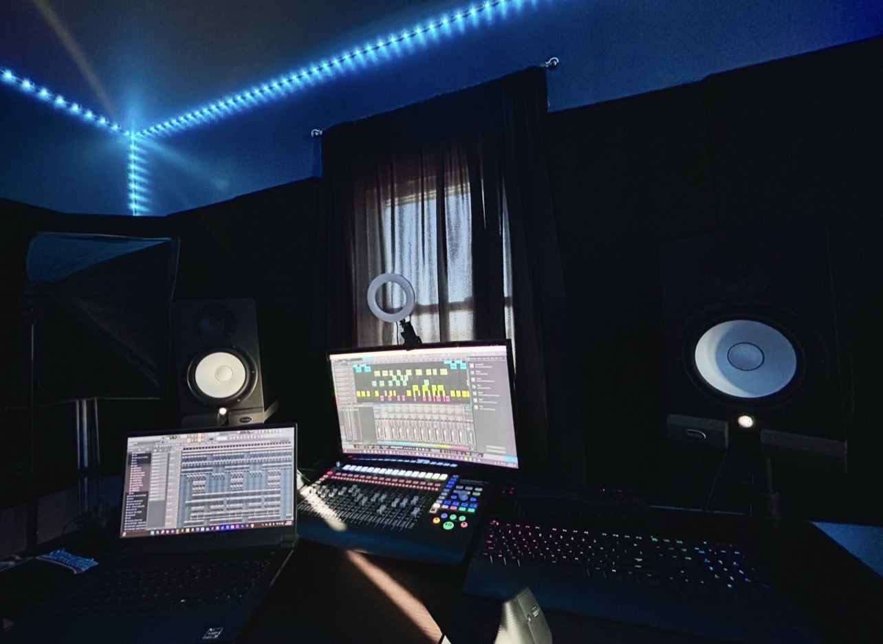 Music studio with computer screens, speakers, and sound equipment in a dark room with blue lighting.