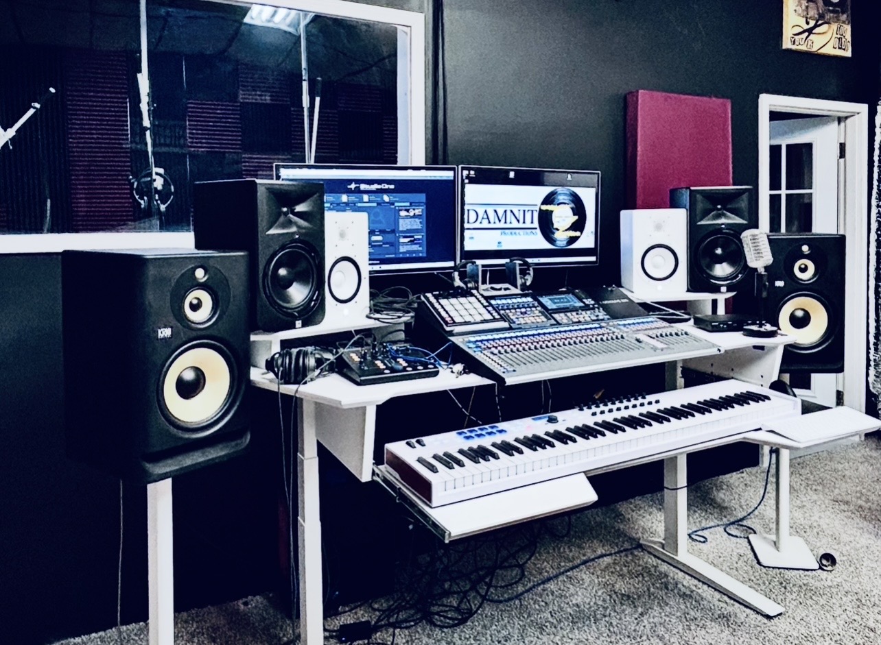 Music studio with speakers, mixing console, keyboard, and computer monitor in a room with dark walls.