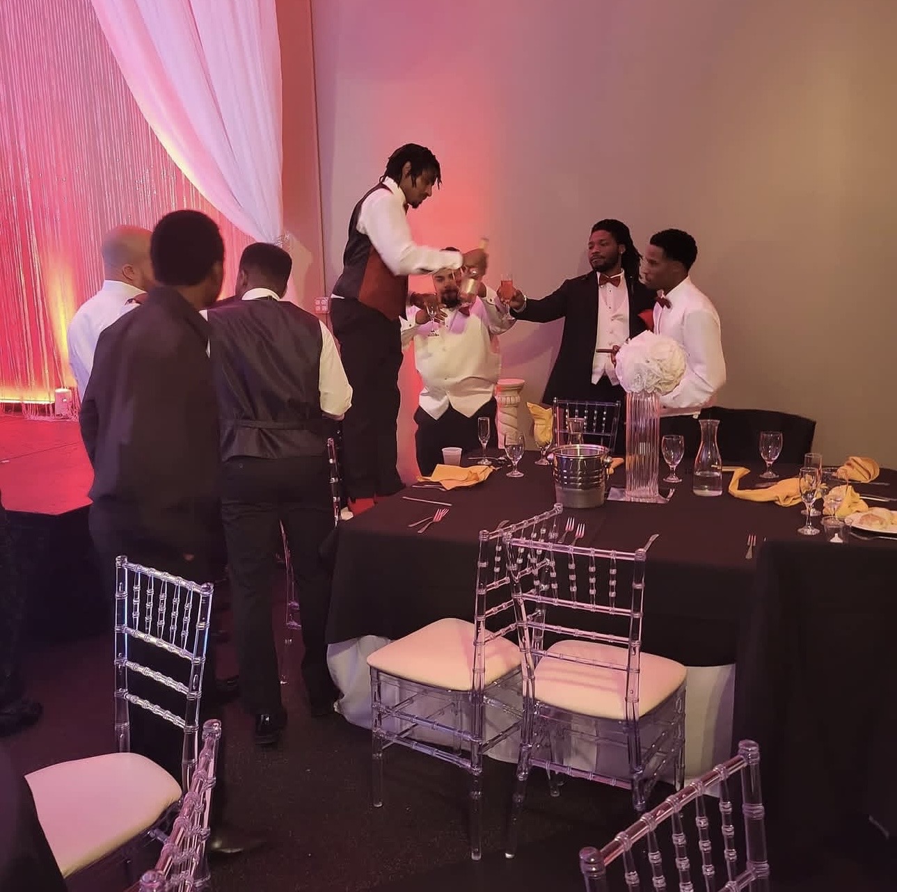 Group of people around a table at a celebration, with a person serving drinks, decorated with flowers and tableware.