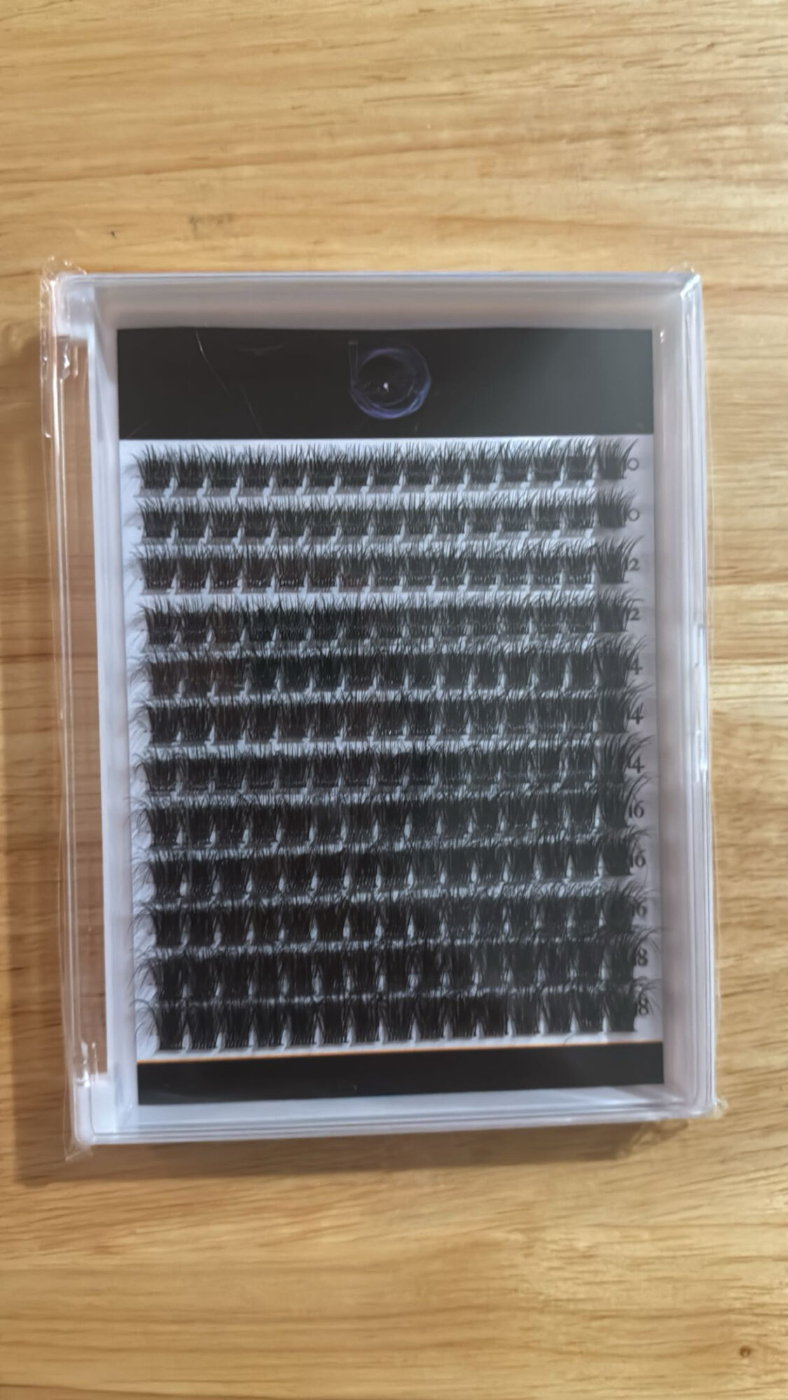 A clear plastic case with black and white eyelash extensions inside, placed on a wooden surface.