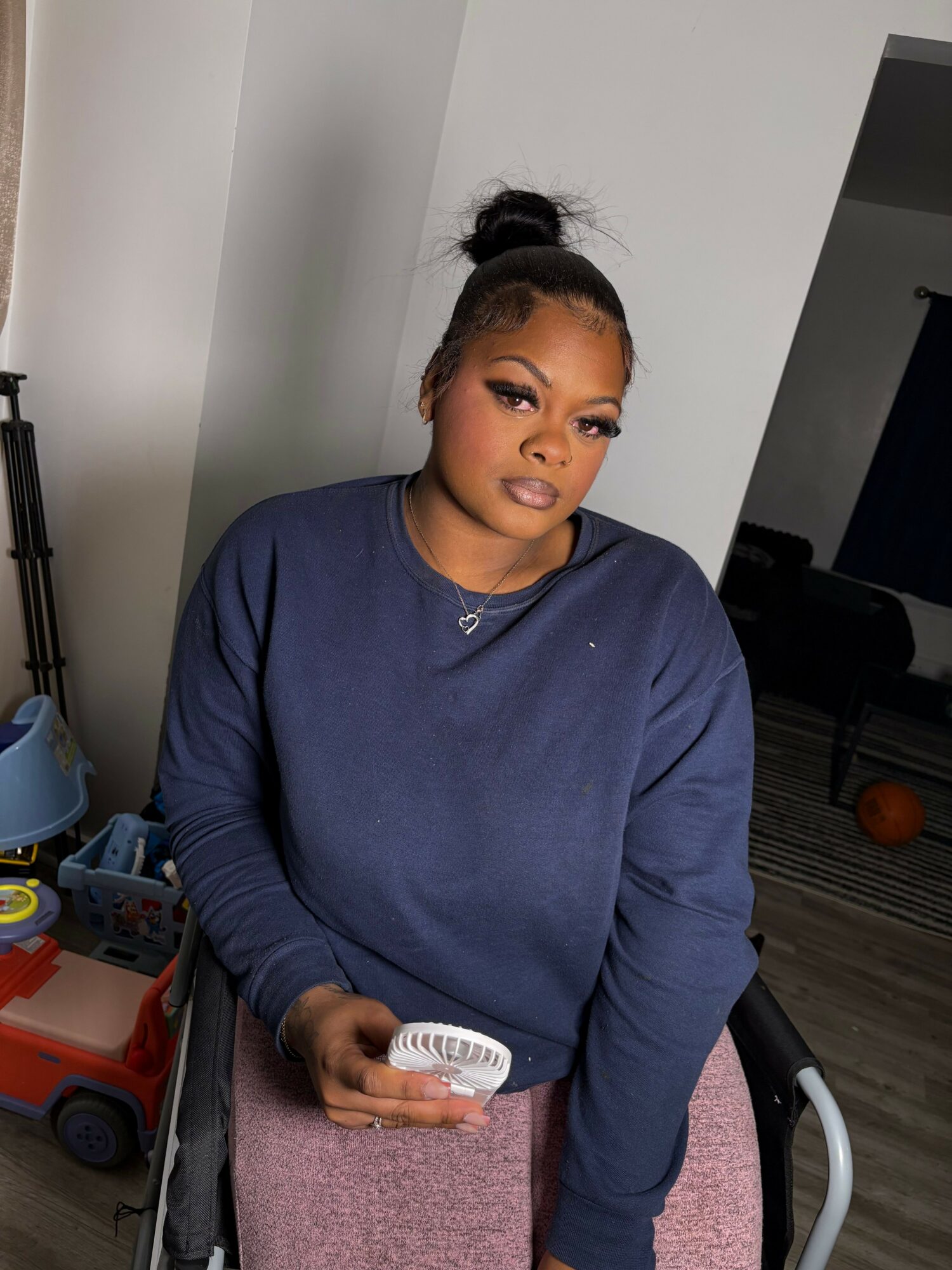 Woman with dark hair in a bun, wearing a navy blue sweatshirt, holding a white object, sitting in a room.