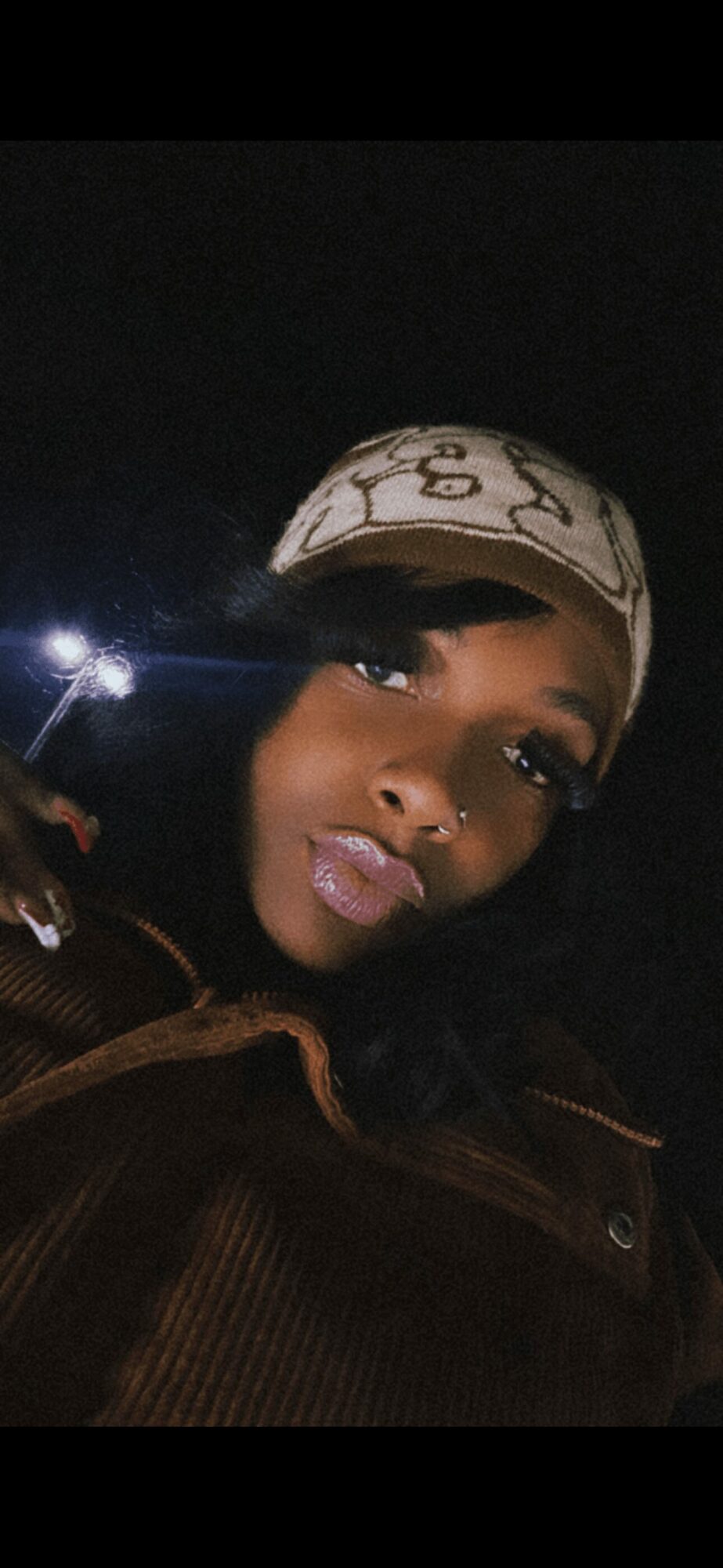 Person wearing a patterned headscarf and dark clothing, with a dark background, illuminated by a light source.