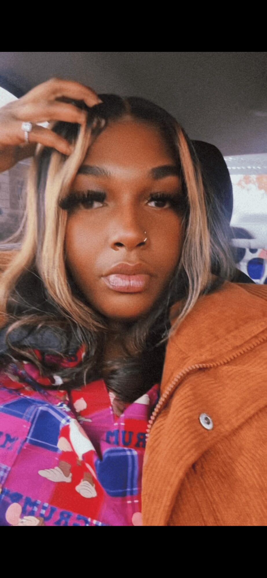 Close-up of a woman with long hair, wearing a colorful jacket, sitting in a vehicle.