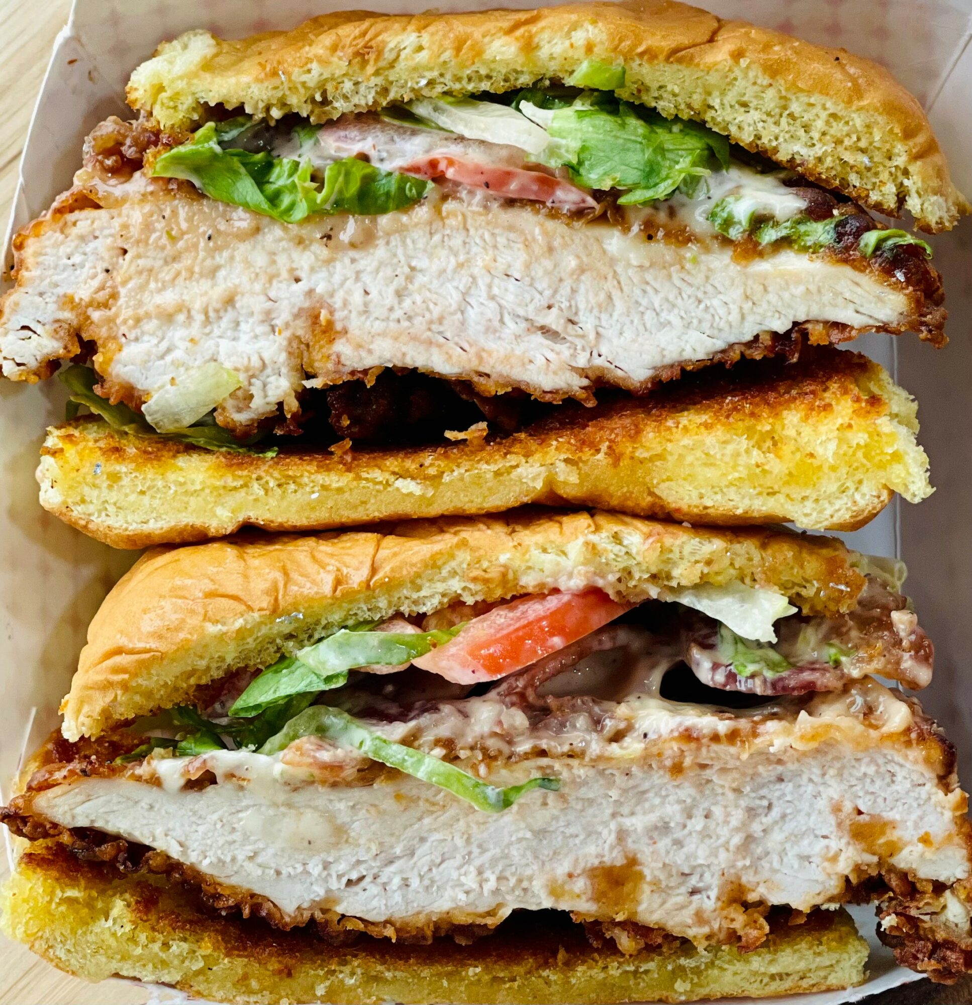 Two sandwiches with fried chicken, lettuce, tomato, and sauce, cut in half, showing fillings and bread. Word count: 20