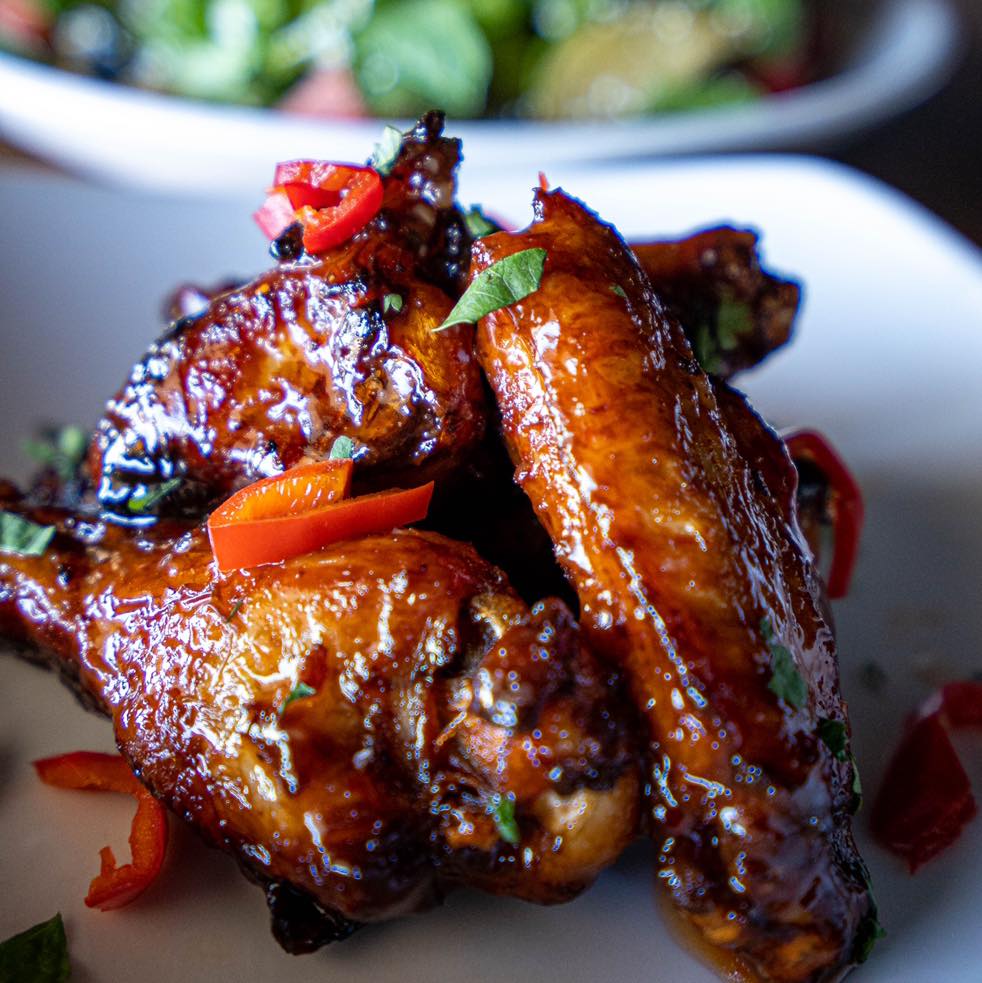 Close-up of glazed chicken wings garnished with chopped red peppers and green herbs on a white plate.
