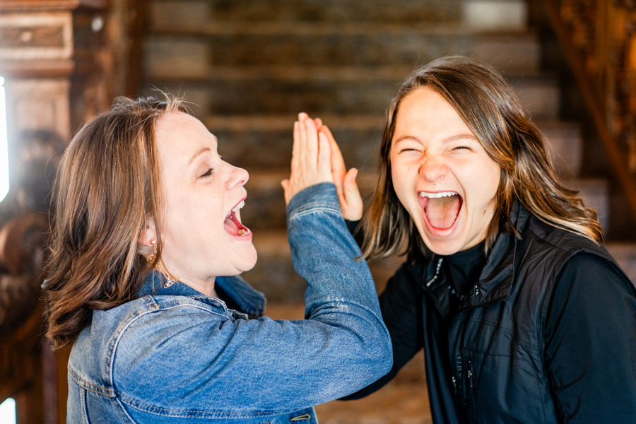 Two women smiling and high-fiving each other indoors, with a wooden background.