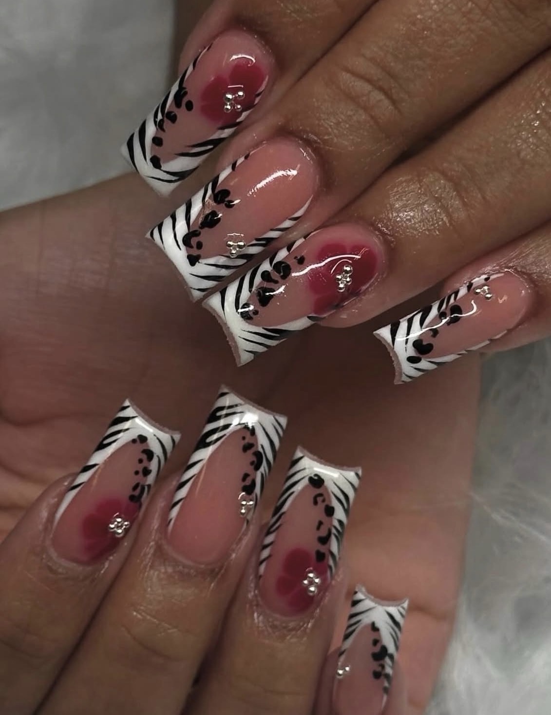 Nail art with pink and black floral design on white tips, decorated with small rhinestones, on long, square-shaped nails.