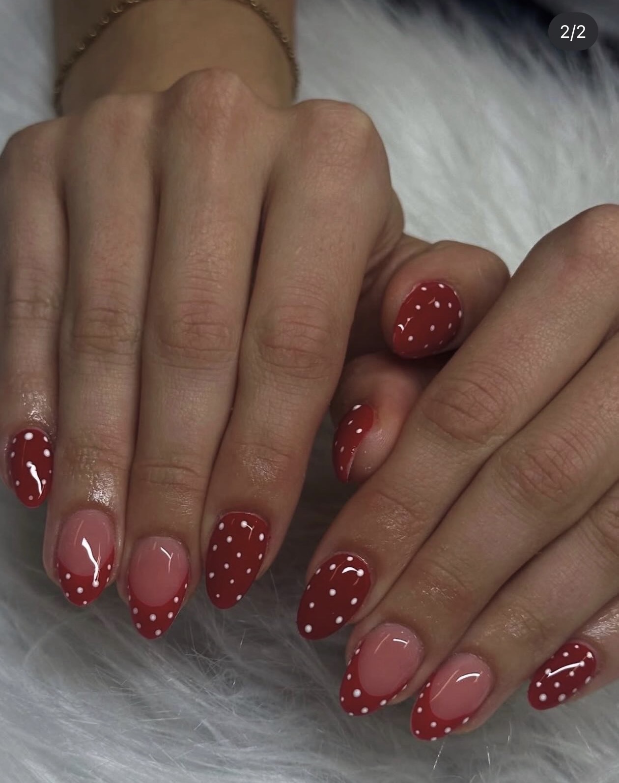 Two hands with manicured nails, some nails painted red with white polka dots, others with clear polish and red tips.