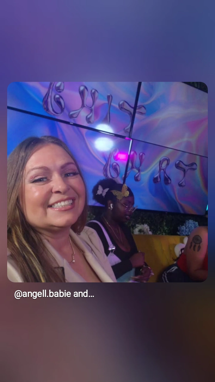 Two women smiling in front of a colorful, abstract digital display, with one woman in the foreground and the other in the background.