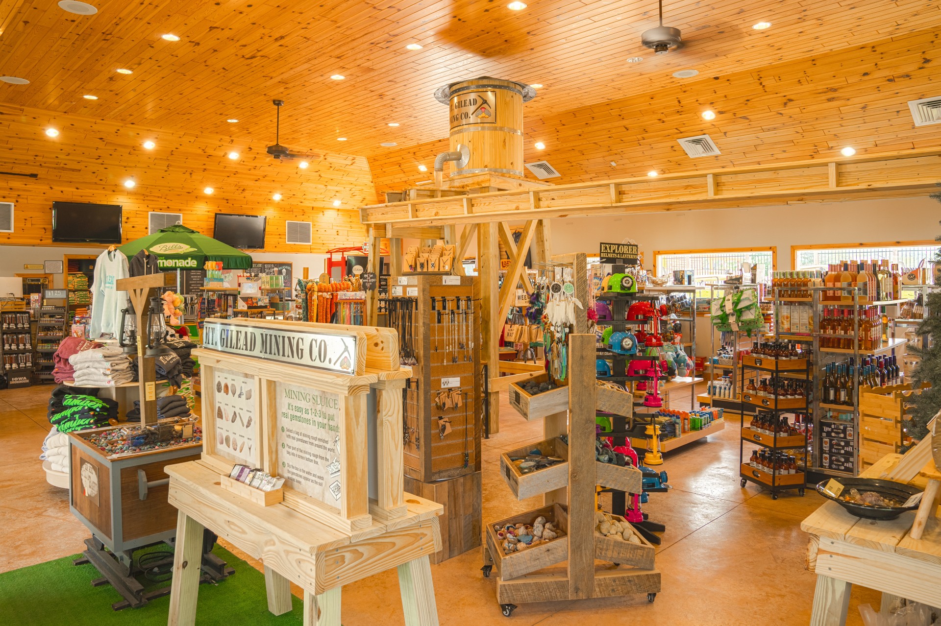 Interior of a store with wooden walls and ceiling, shelves stocked with various products, and a display table in the foreground.