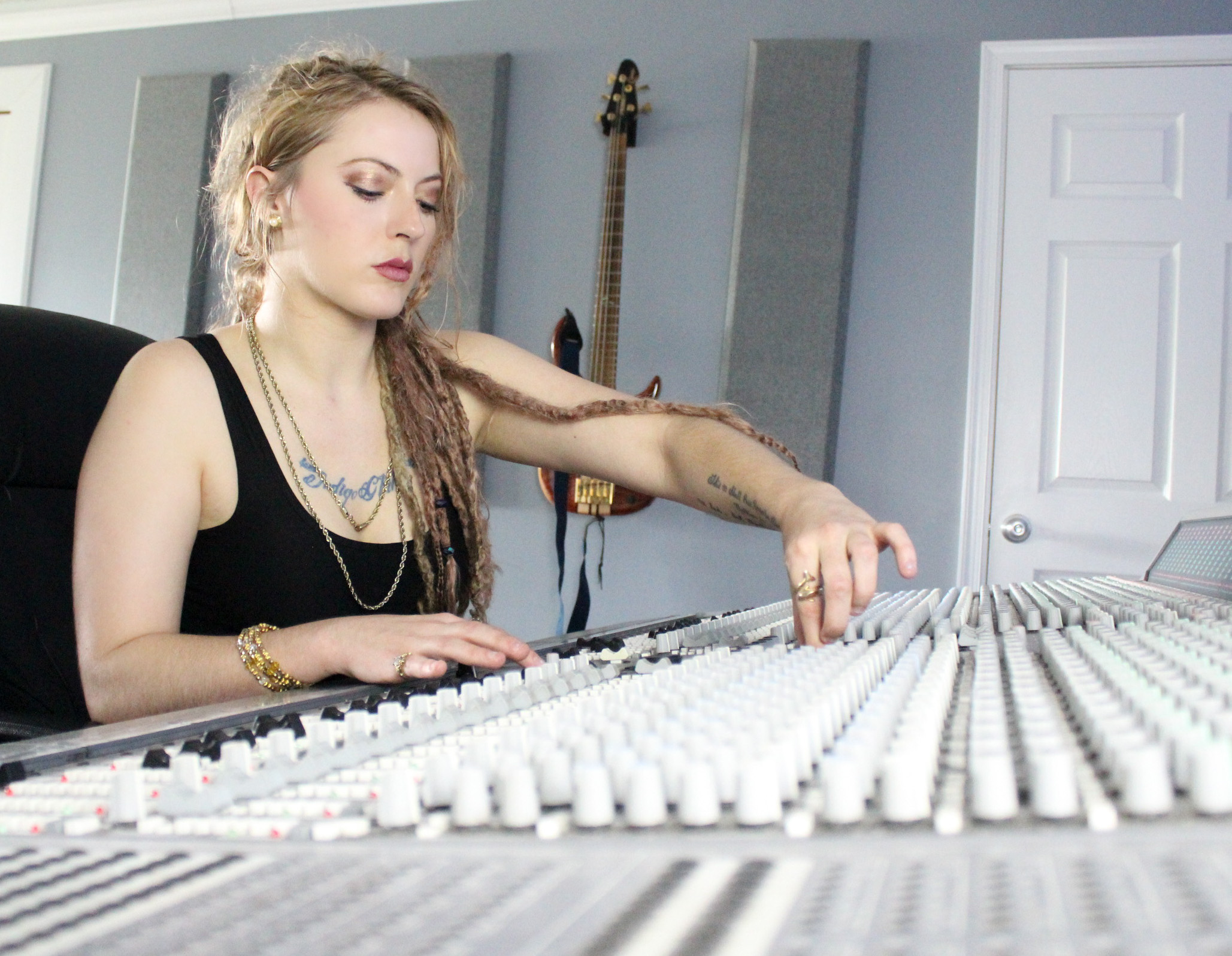 Young woman with long hair and tattoos plays a mixing console in a music studio.