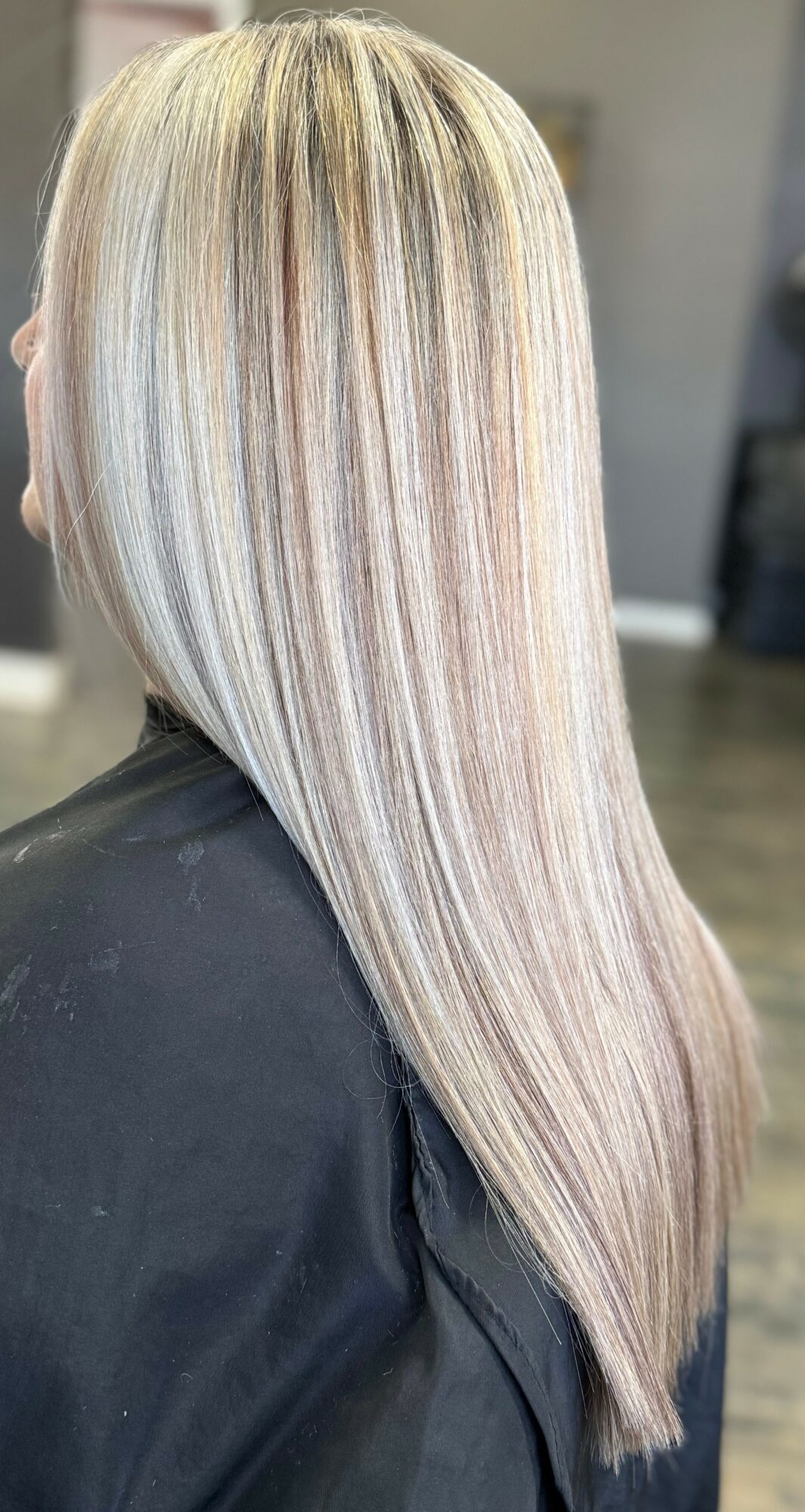 Long, straight, blonde hair with subtle highlights, viewed from the back, in a salon setting.