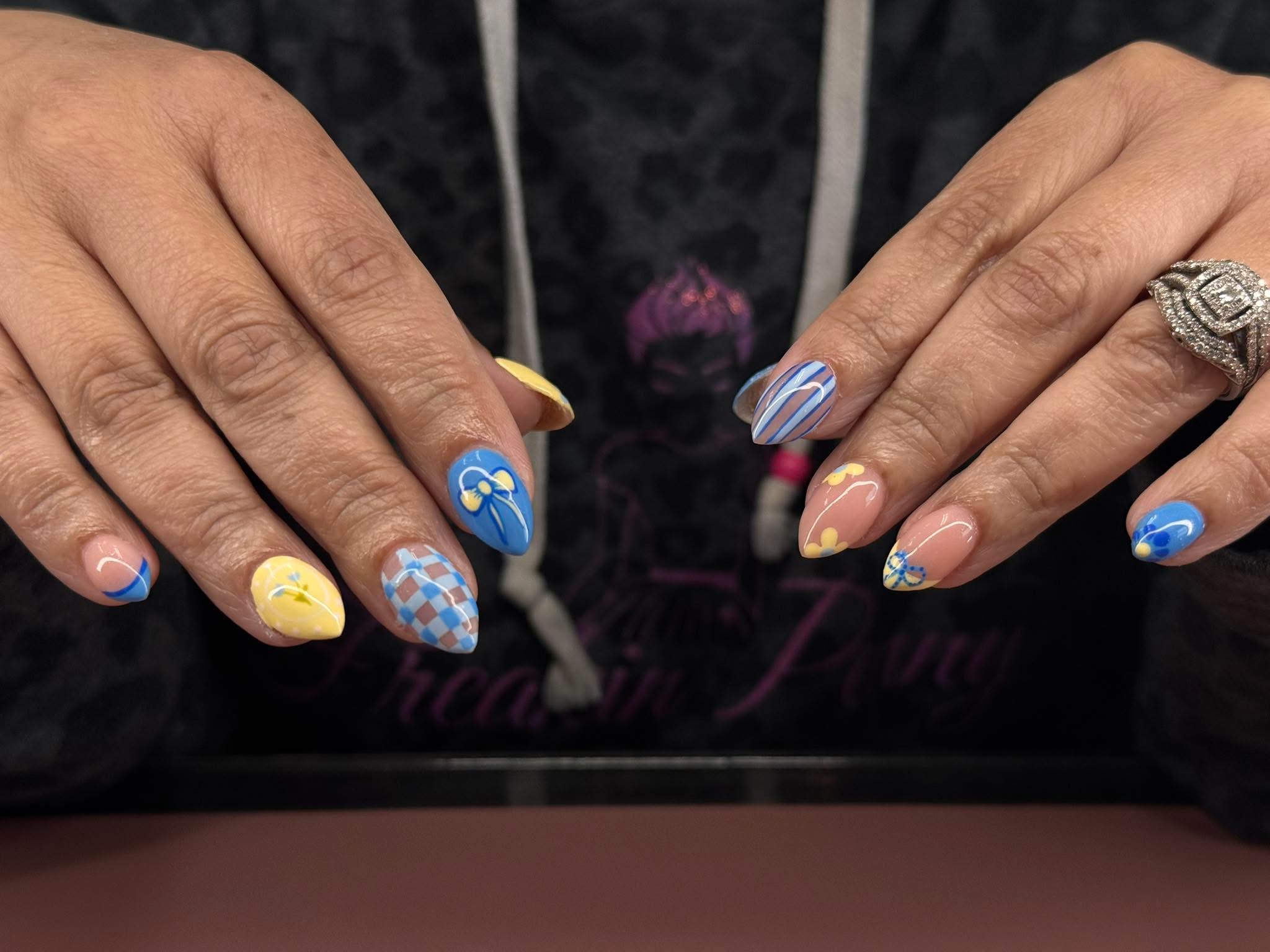 Close-up of hands with colorful, decorated nails, rings, and a dark patterned shirt in the background.