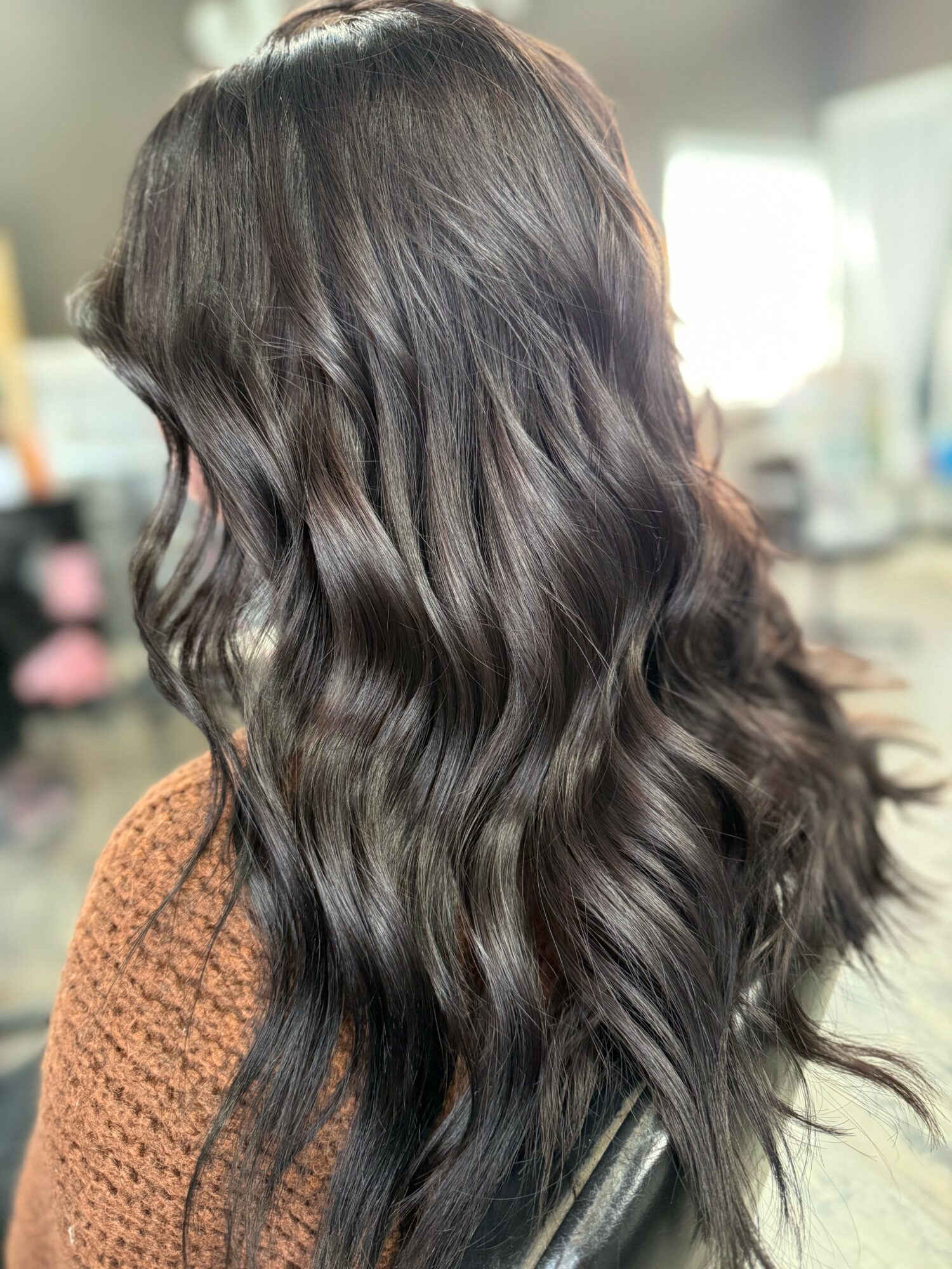 Side view of a person with long, wavy, dark brown hair in a salon setting.