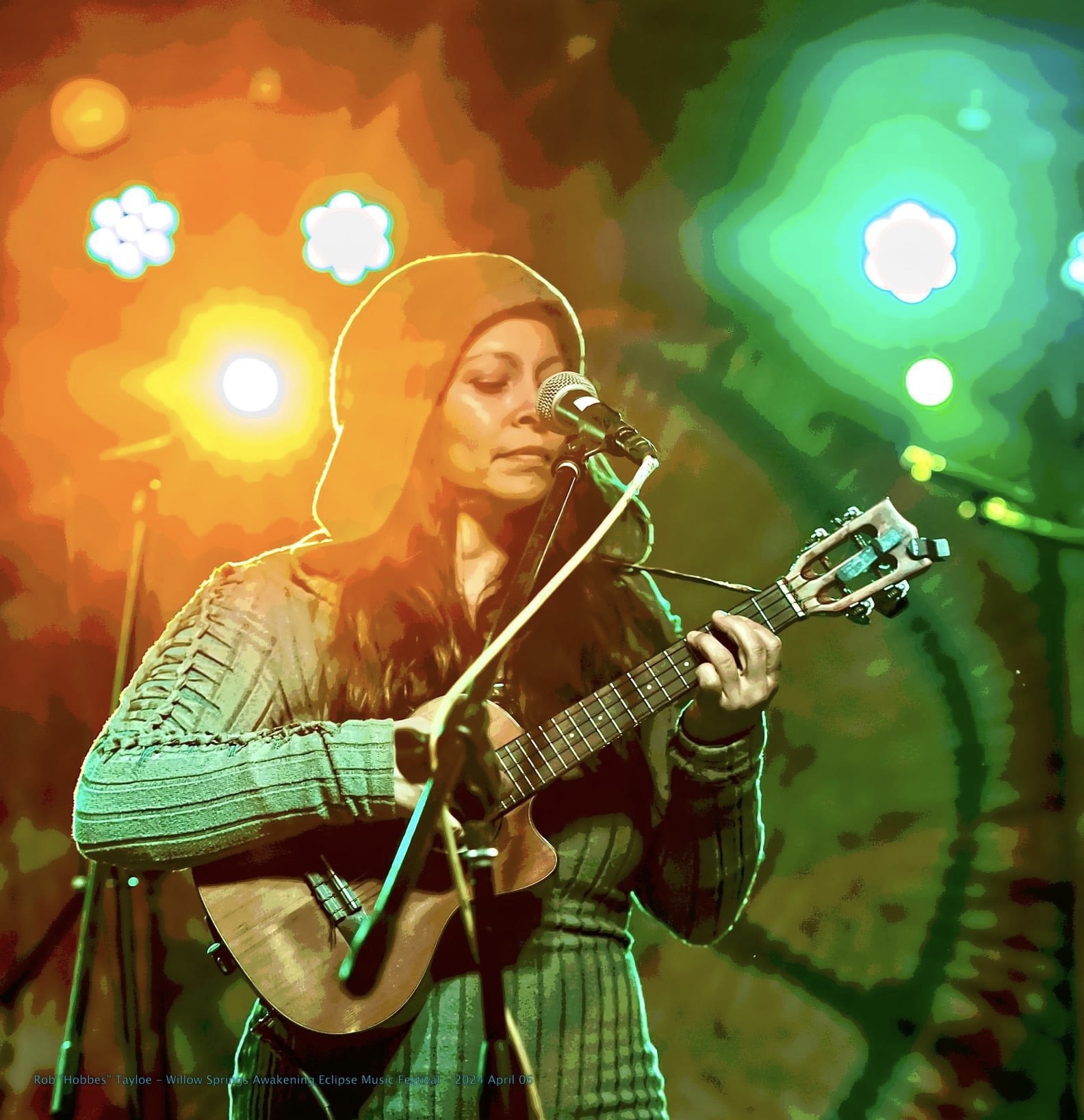 Woman playing guitar and singing into microphone on colorful stage with bright lights.