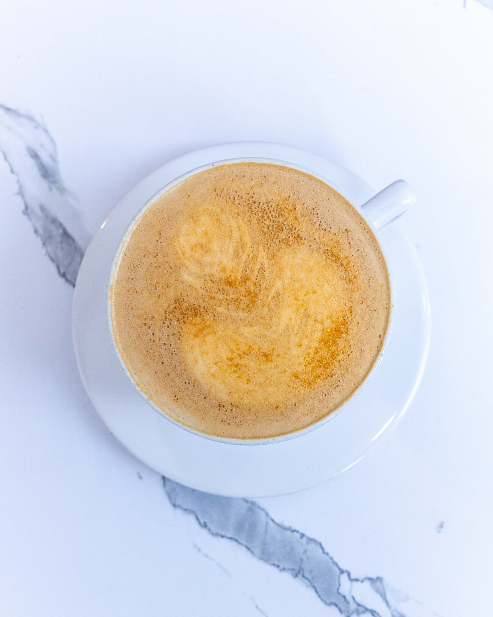 Top view of a cup of frothy coffee on a white saucer, placed on a marble surface.