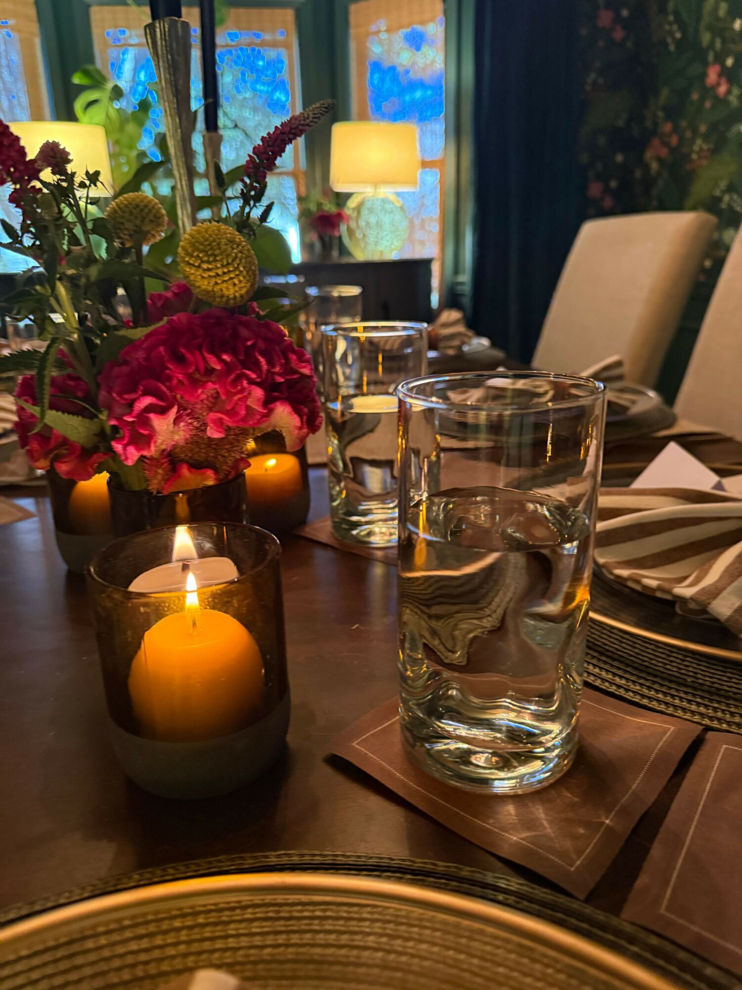 Table setting with glasses, candles, and a floral centerpiece in a dining room.