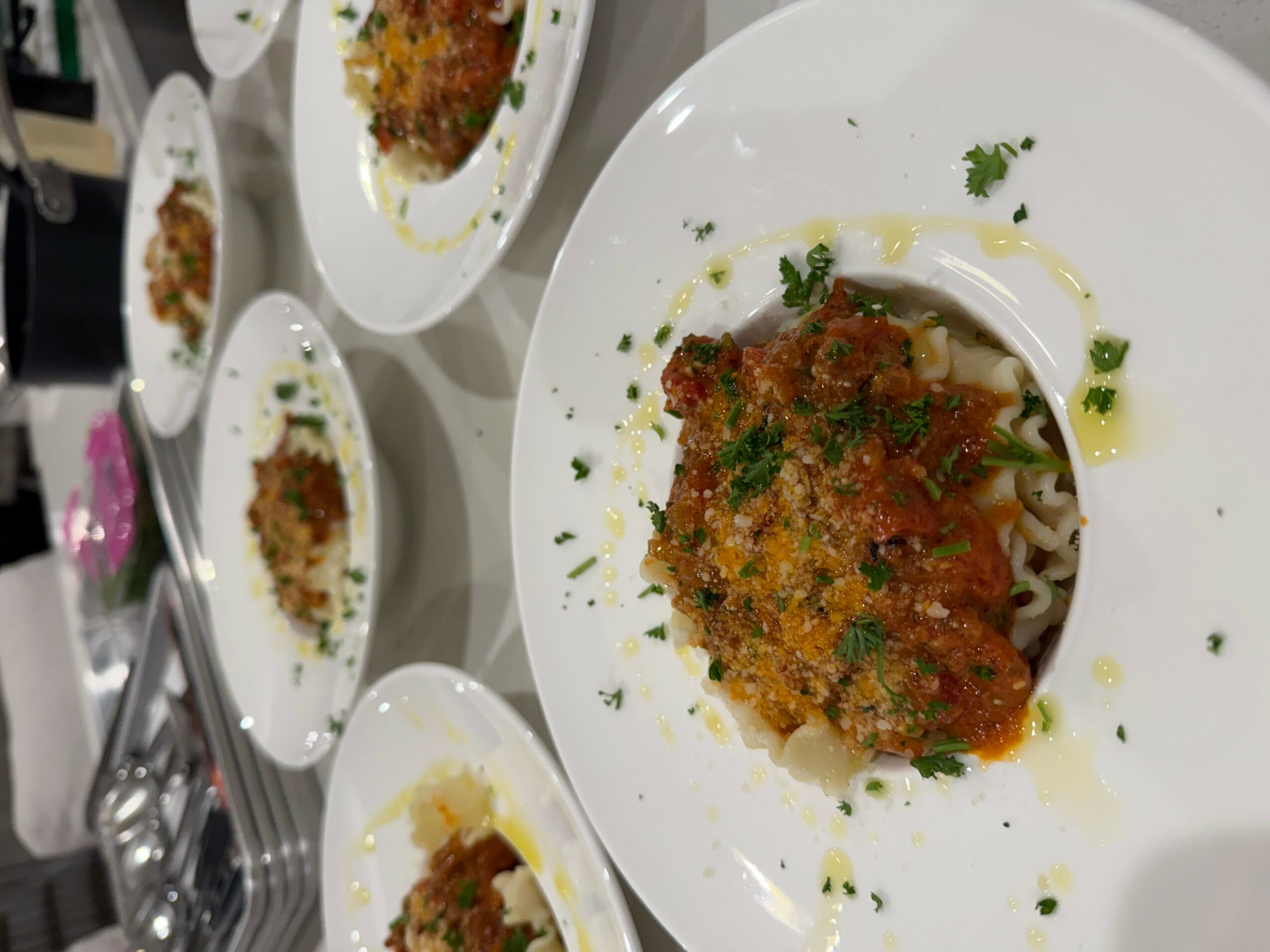 Plate with breaded fried fish fillet garnished with herbs and sauce, on a white plate with other similar dishes in the background.