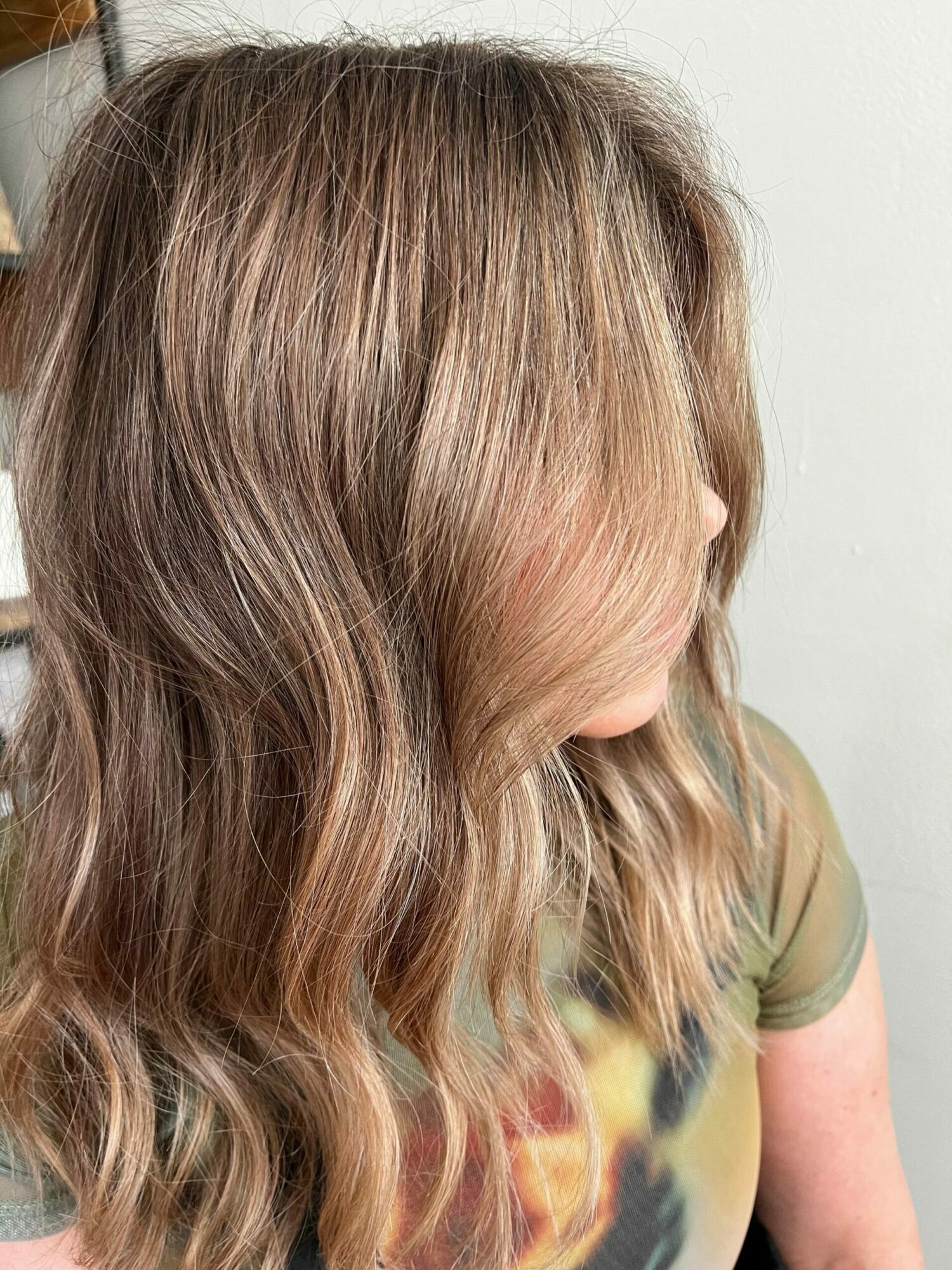 A person with long, wavy, light brown hair lying sideways, wearing a green shirt with a colorful design, against a plain background.