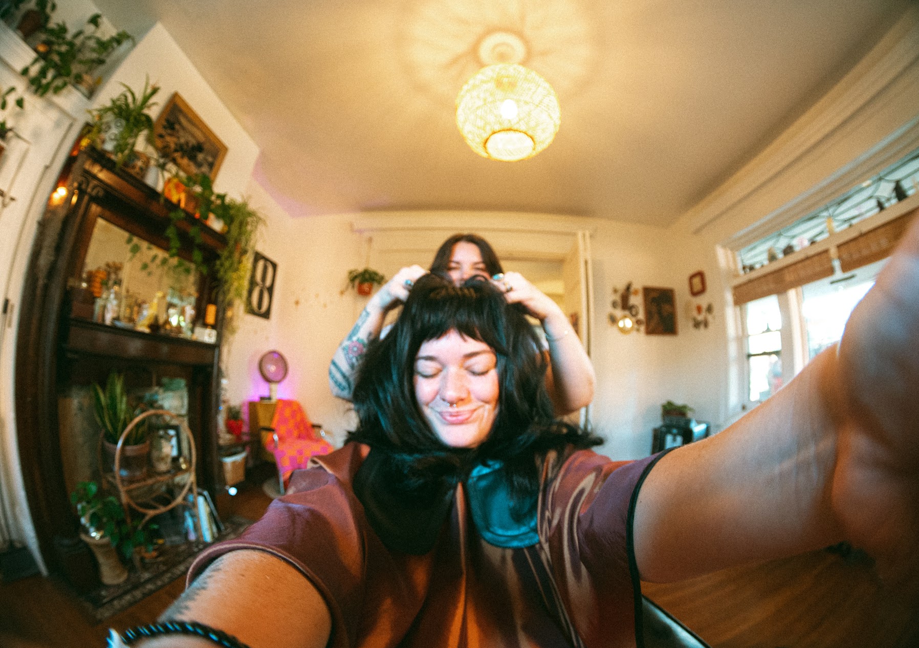 Two women taking a selfie in a cozy living room, one with black hair and the other with glasses, smiling.