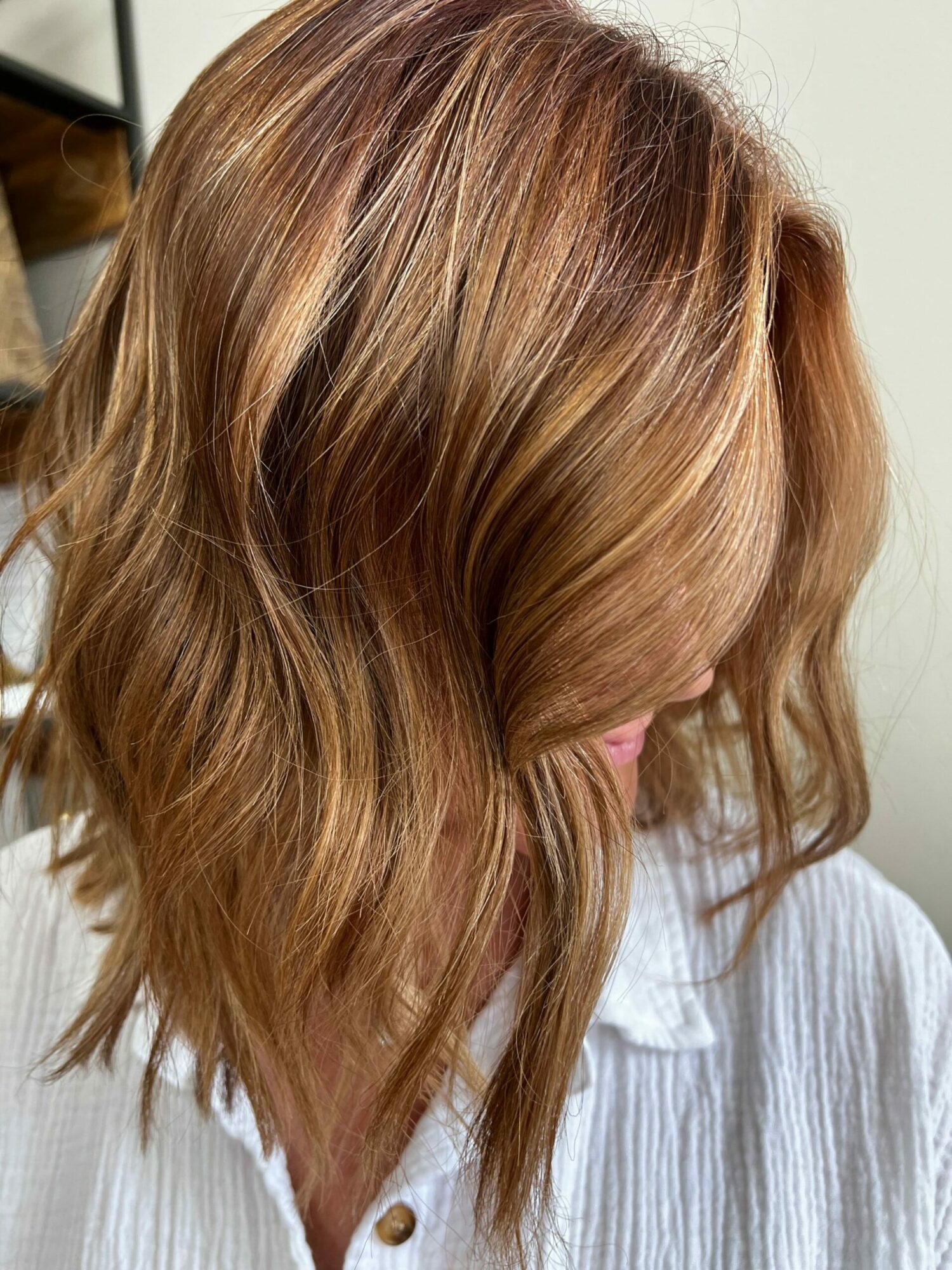 Close-up of a person's head with wavy, light brown hair, wearing a white shirt, facing sideways.