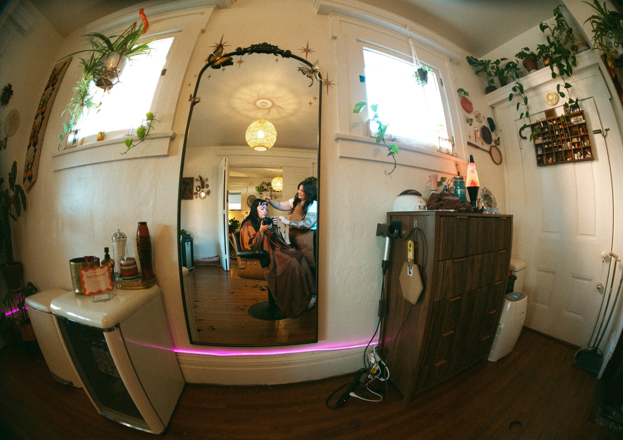 Living room with windows, plants, and furniture reflected in a mirror, fisheye lens effect, pink LED strip, and various objects.