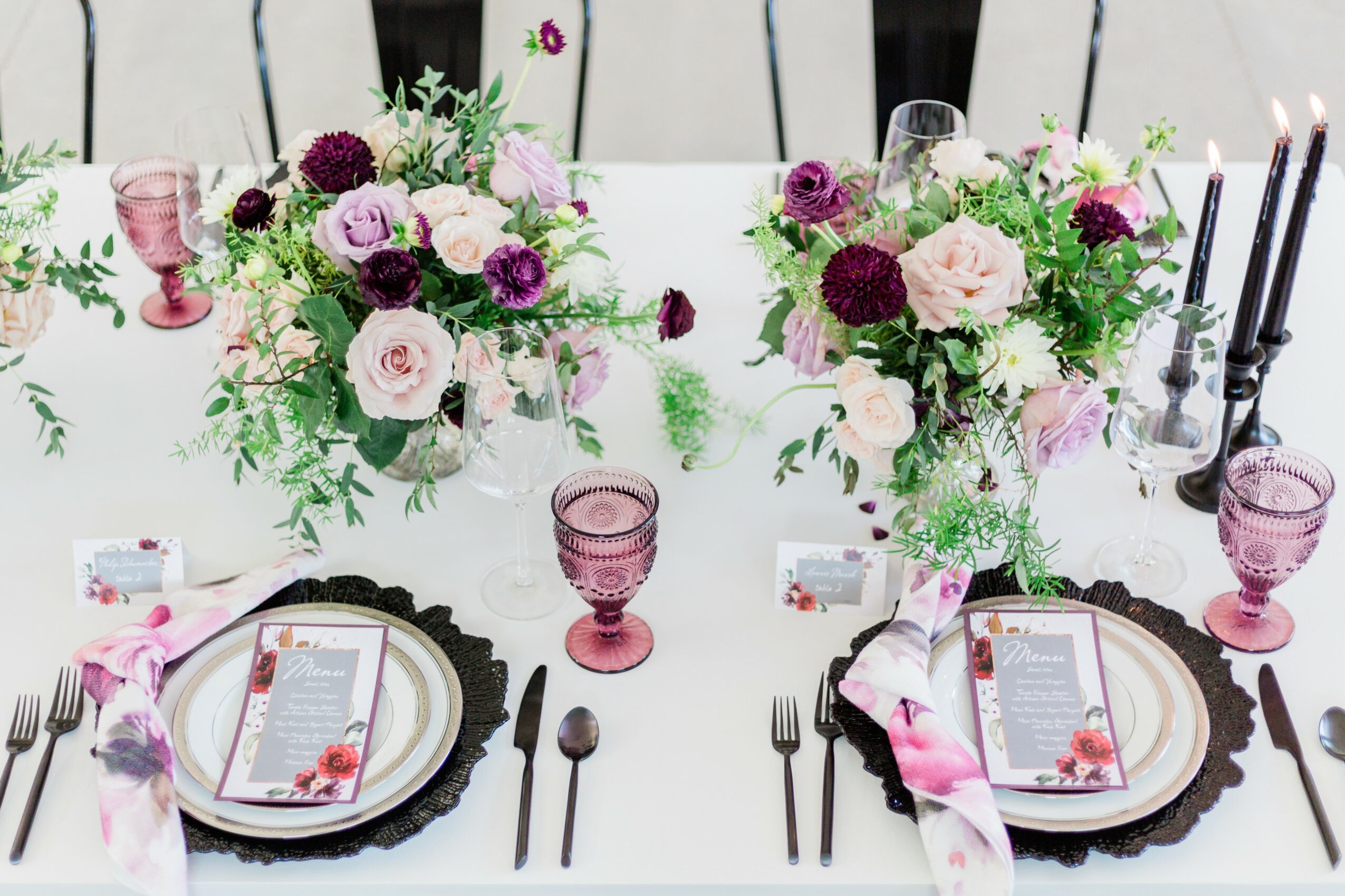 Table with floral centerpieces, pink glasses, black and white plates, and pink napkins, set for a formal event.
