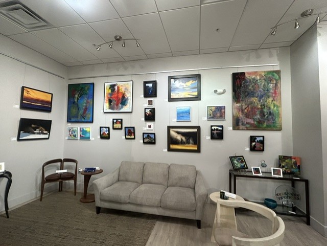 Gallery wall with colorful paintings and photographs, beige sofa, two chairs, and a small table in a modern room.