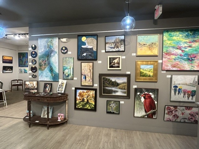Gallery wall with various framed paintings and photographs, a small table with art supplies, and a disco ball hanging from the ceiling.