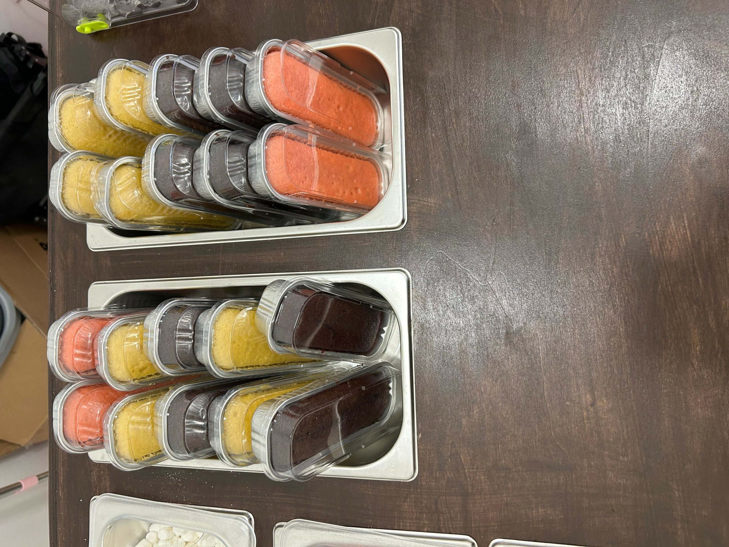 Three white trays with small jars of yellow, orange, and dark-colored spreads on a wooden surface.