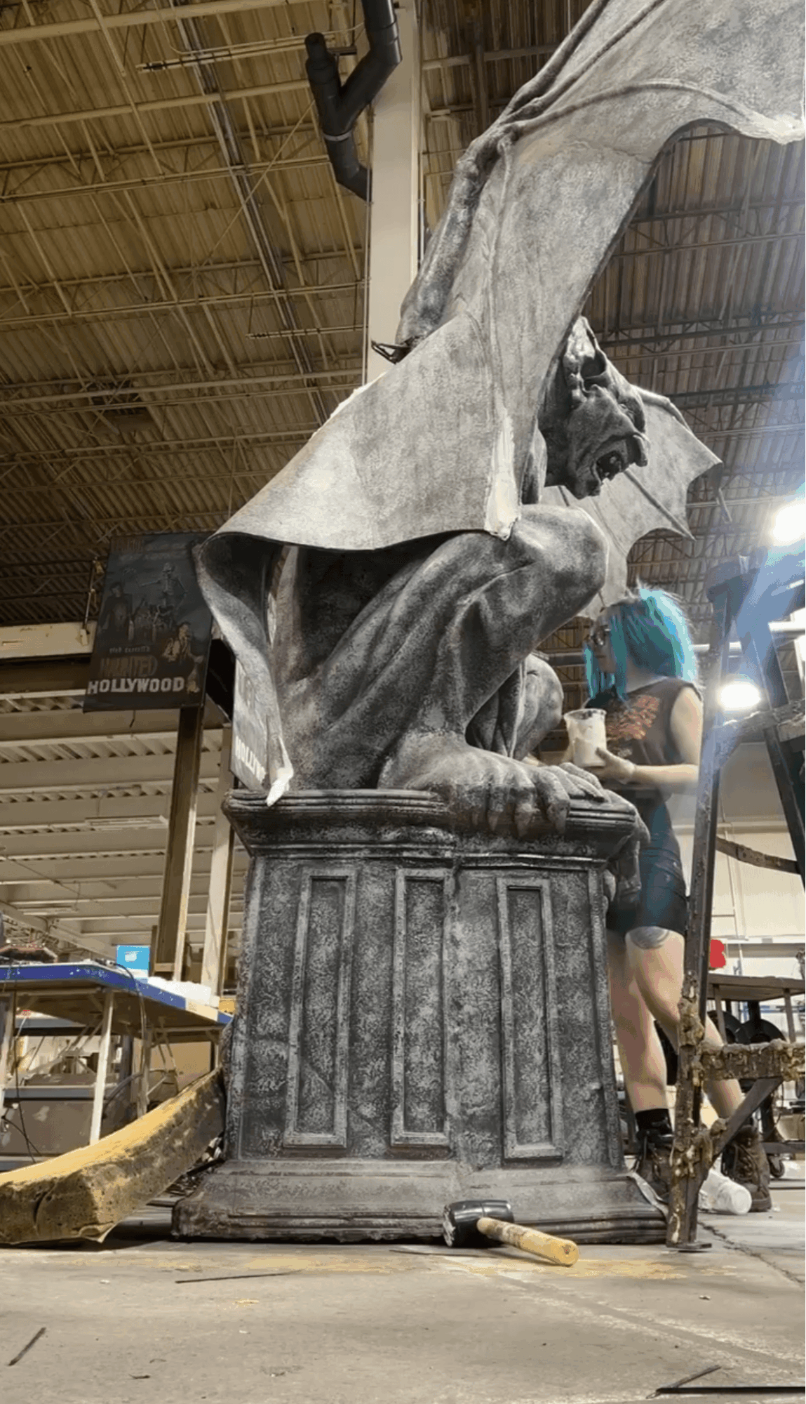 Large stone sculpture of a lion with a cloth draped over its head, situated indoors with people nearby.