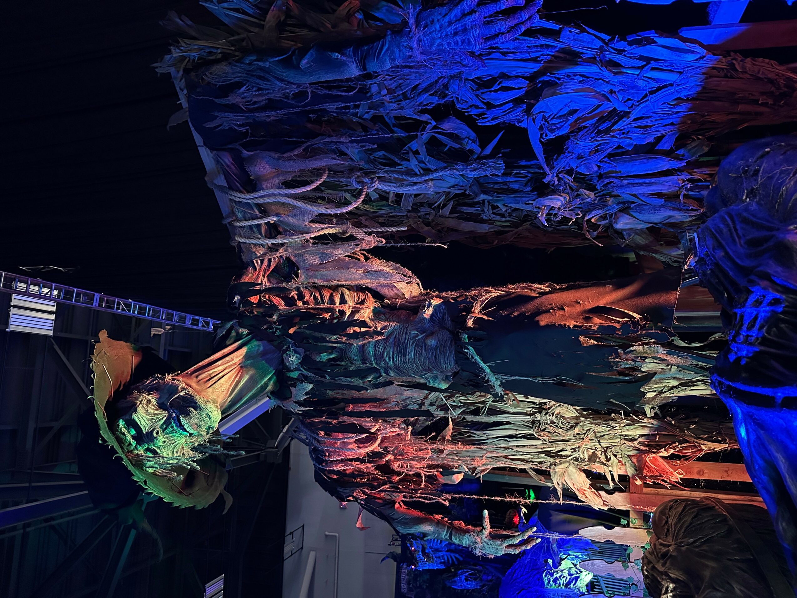 People are in a dark room with colorful lighting, and a large textured fabric or installation overhead.