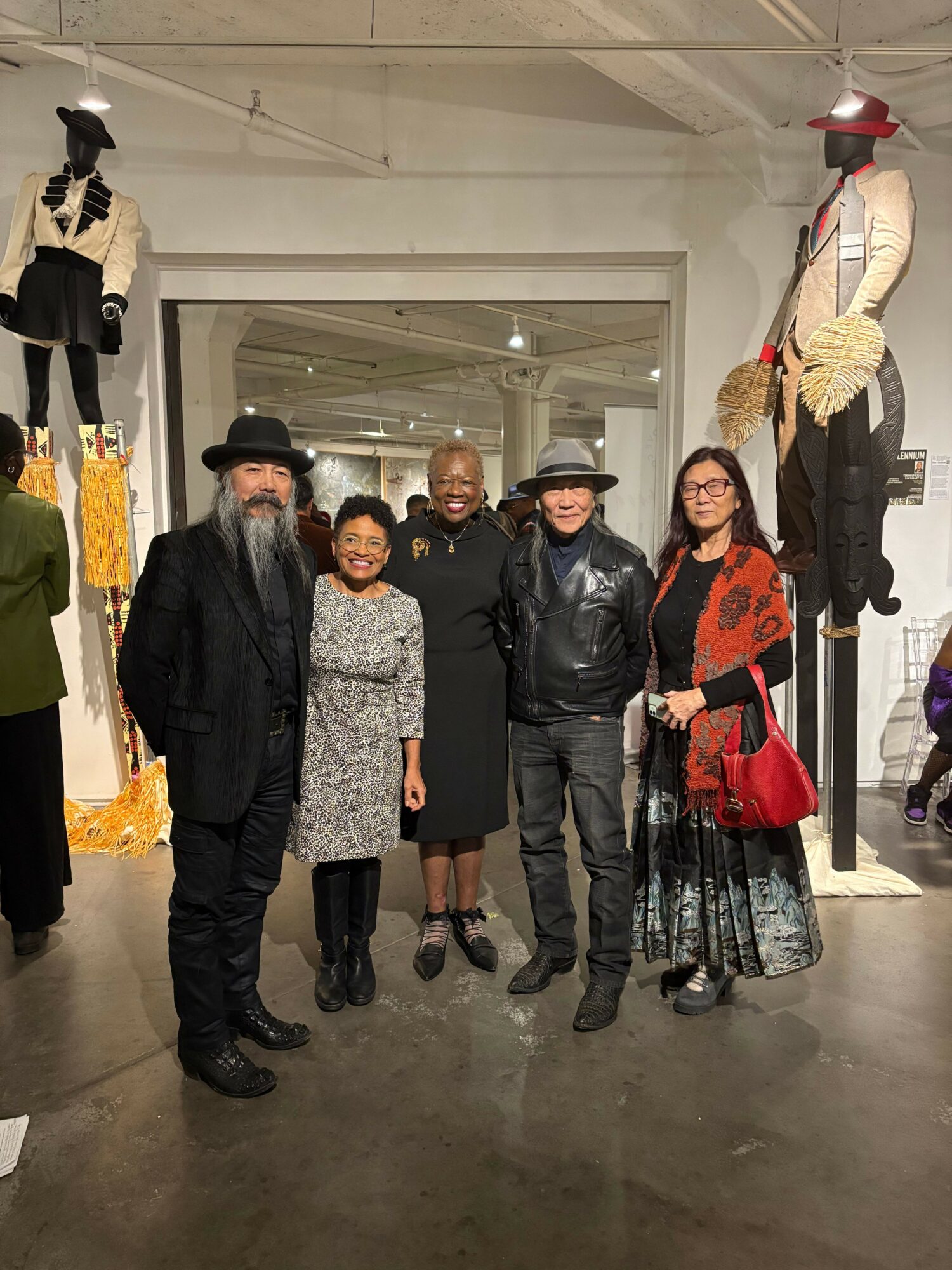 Four people standing in a hallway with mannequins dressed in clothing behind them, some wearing coats and scarves.