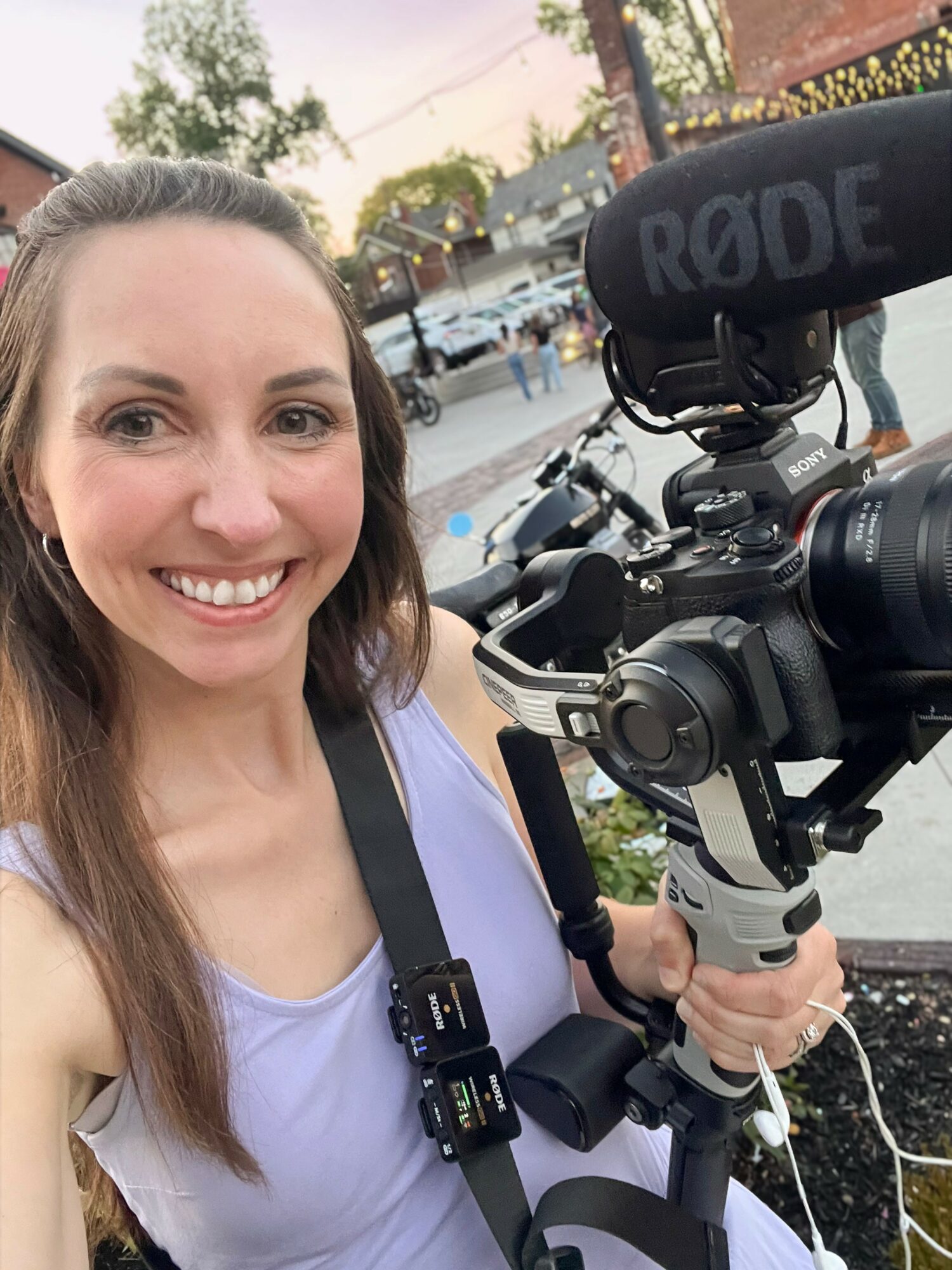 Woman smiling holding professional video camera outdoors during daytime.