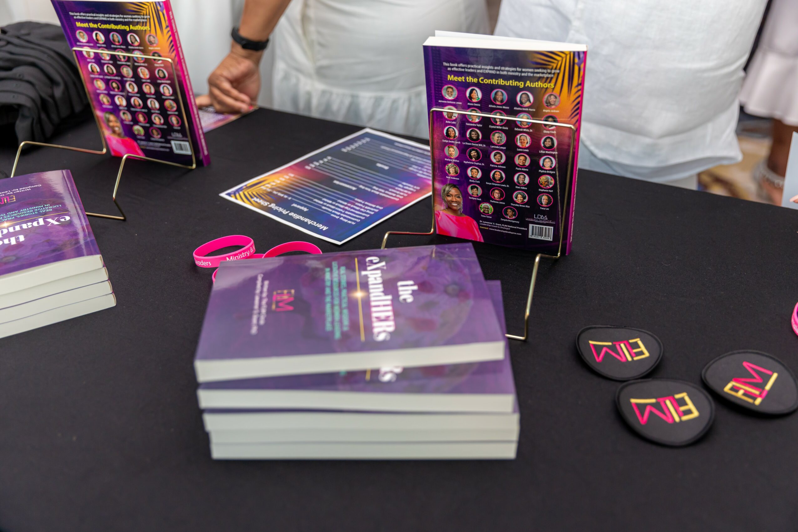 Table with stacks of colorful booklets, round tokens, and informational flyers, with people in the background.