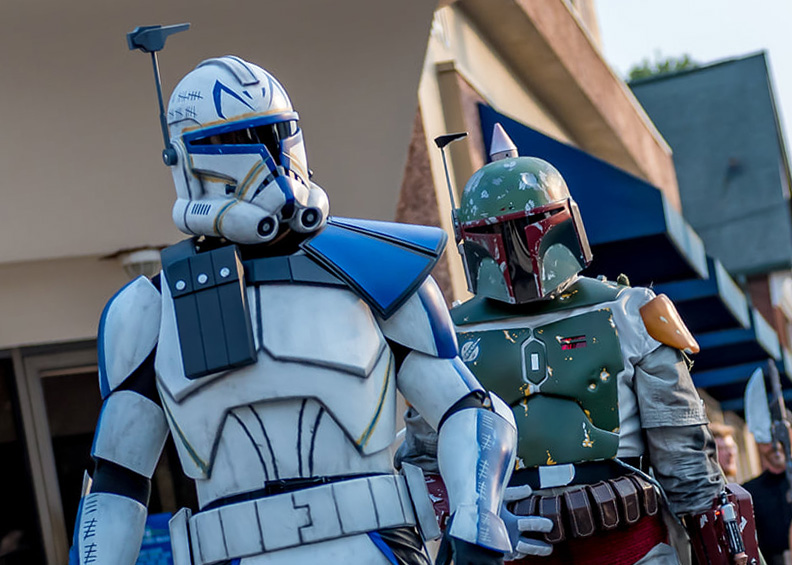 Two people dressed as Star Wars characters, a clone trooper and Boba Fett, standing outdoors with buildings in the background.