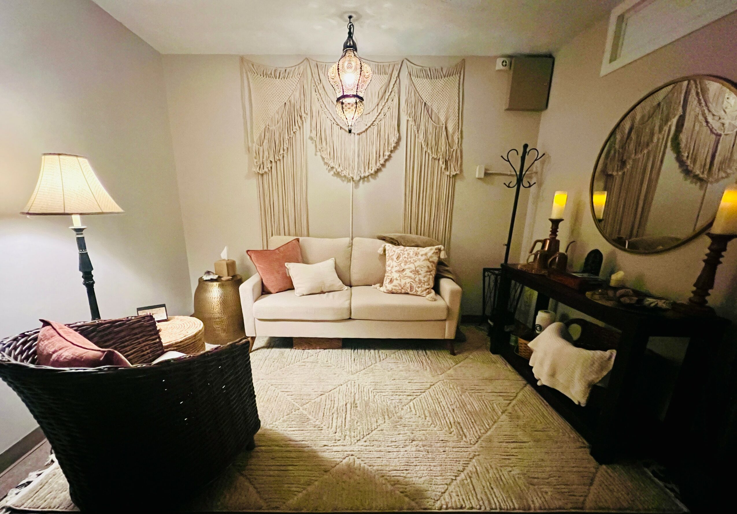 Living room with a white sofa, round mirror, side table, and a black chair, decorated with lamps and curtains.