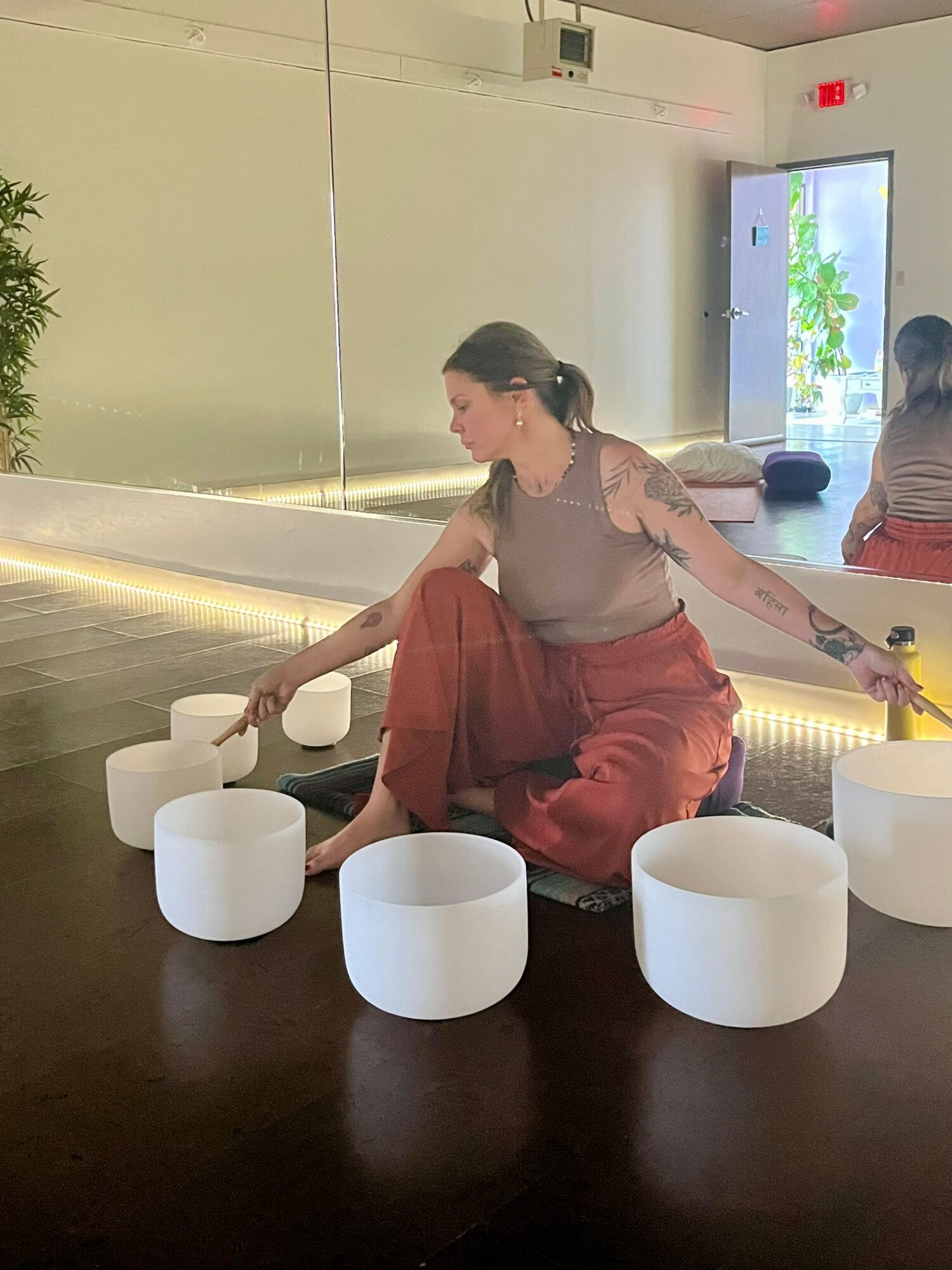Woman sitting on the floor with white circular objects, in a room with a mirror and a window showing trees outside.